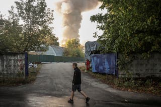 A person passes by the site of a Russian drone strike as smoke rises in the background, amid Russia’s attack on Ukraine, in Kyiv, Ukraine, September 16, 2026.
