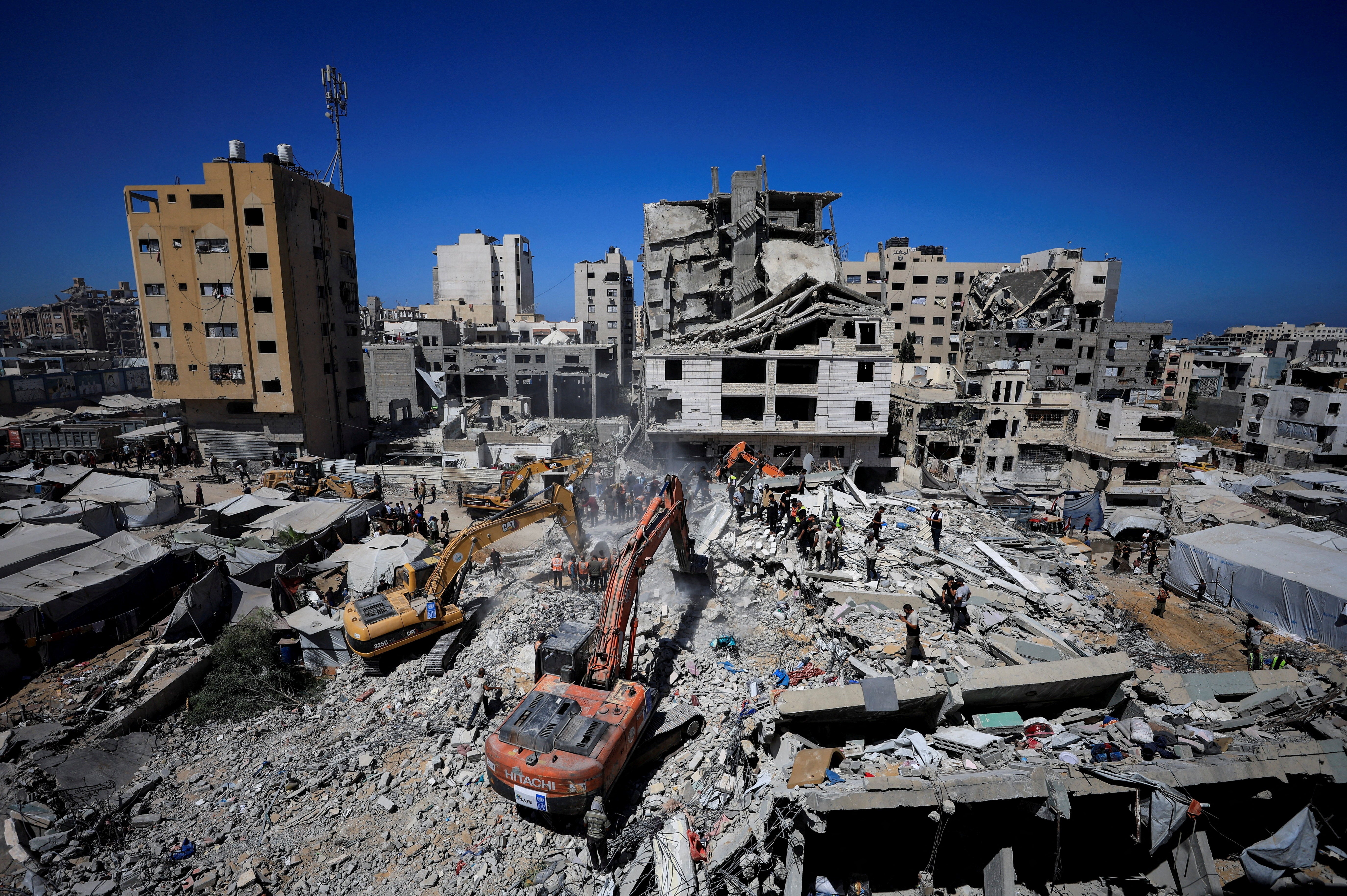 Heavy machinery assists Civil Defence workers attempting to rescue those who are trapped beneath the rubble