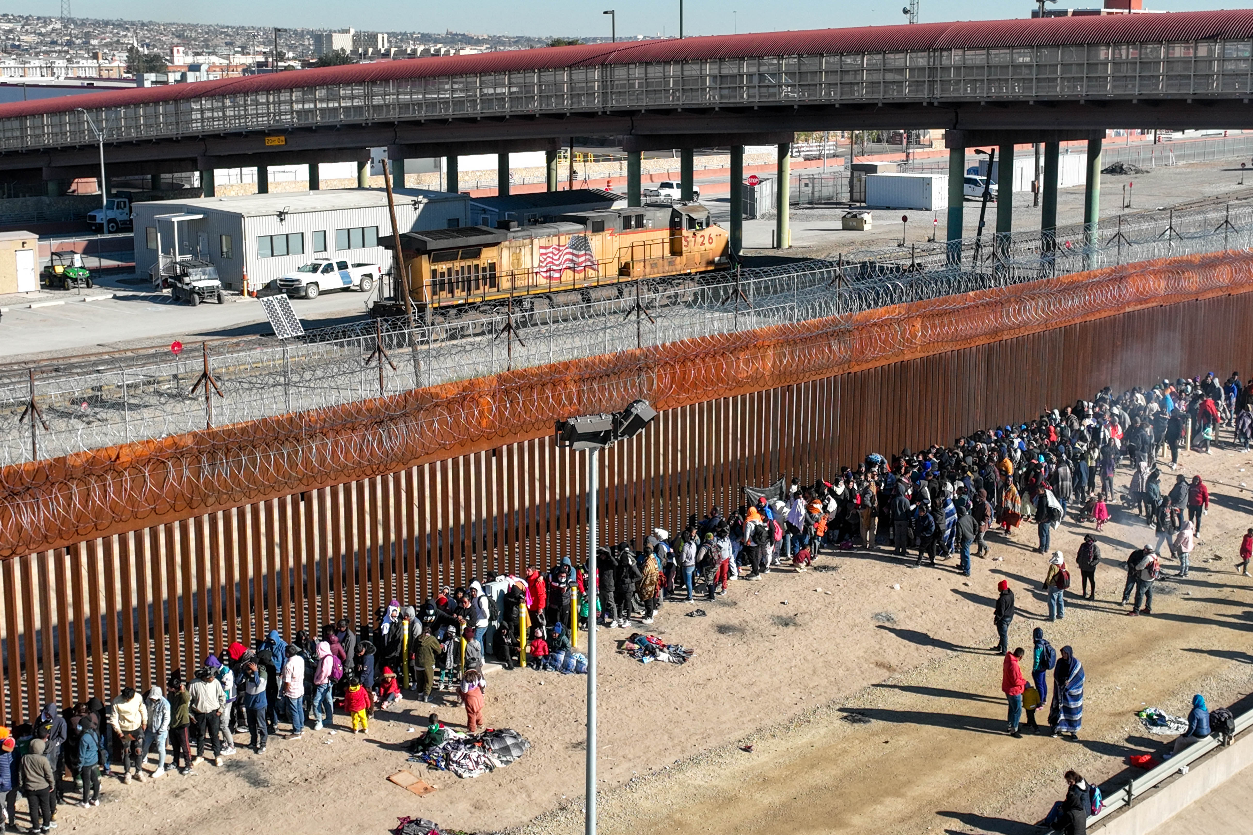 Migrants line up along the U.S. Mexico border fence to apply for asylum in the United States on December 21, 2022 as viewed from Ciudad Juarez, Mexico