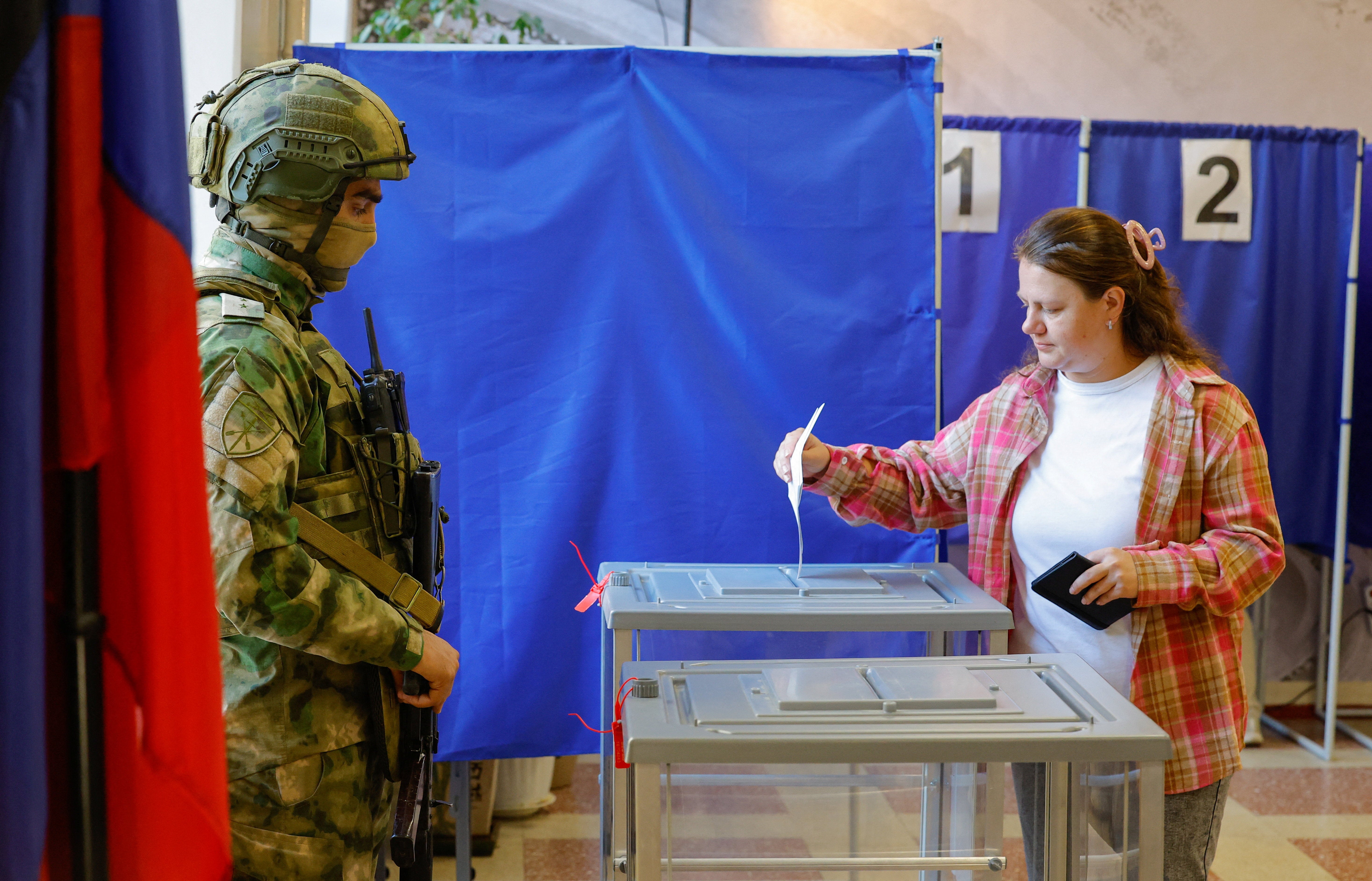 A woman casts her ballot under watch of a serviceman in Russian-occupied Donetsk