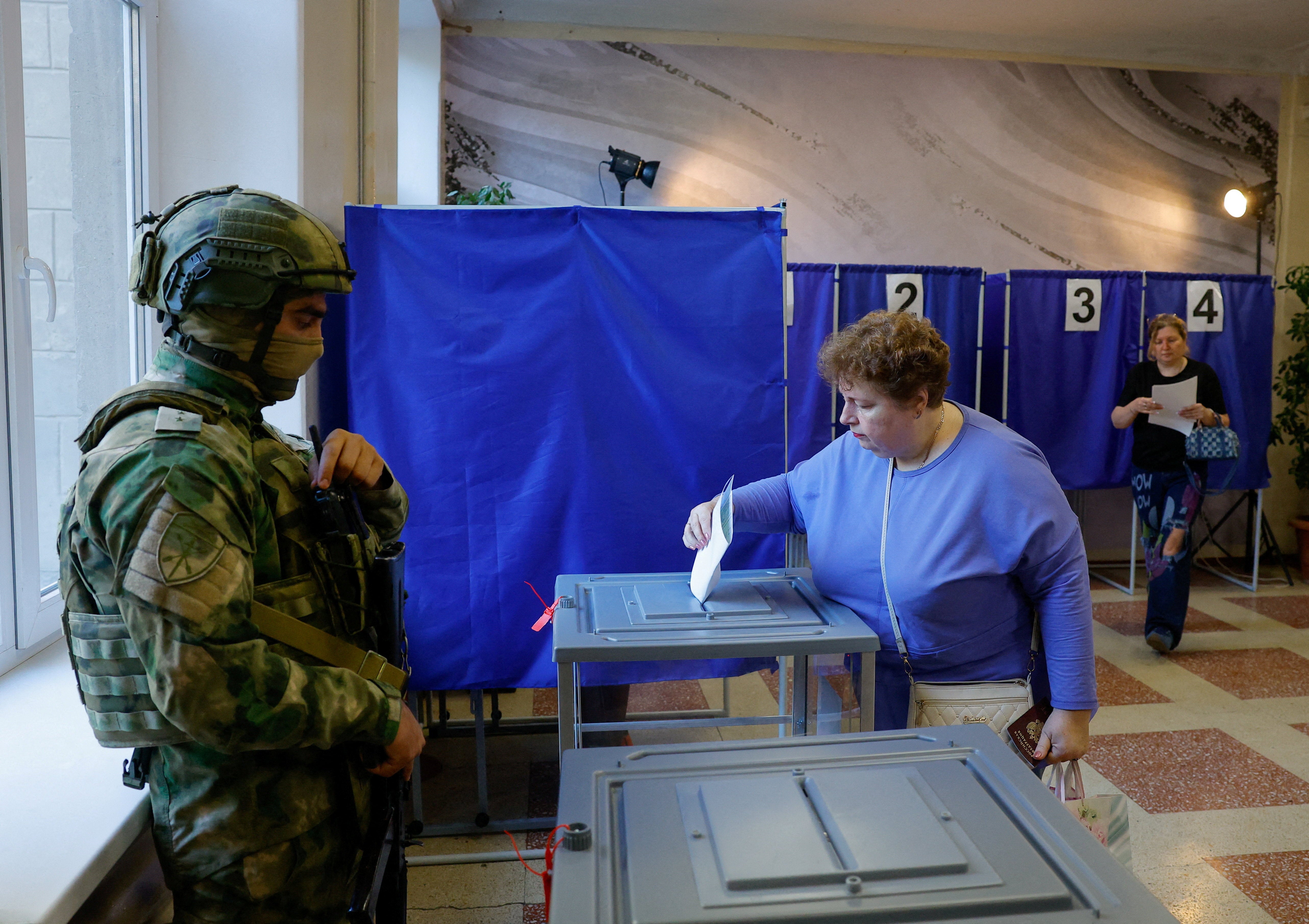 A woman casts her ballot next to a serviceman securing a poling station during Russia's parliamentary elections, in Donetsk, September 18, 2026 (Reuters)