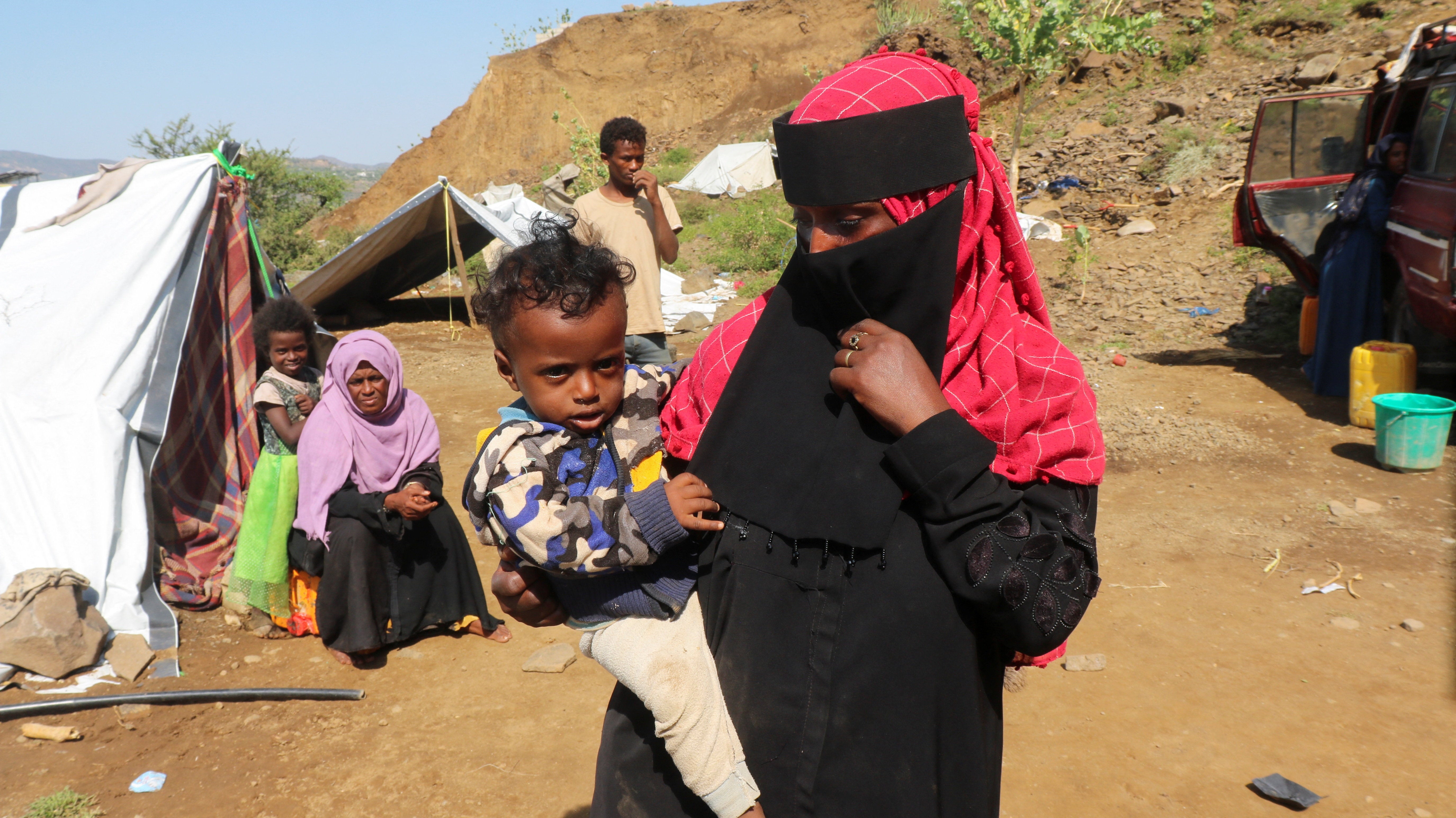 A displaced woman holds a child at a makeshift camp for people displaced by clashes between Iran-aligned Houthi fighters and Saudi-backed Yemeni government forces, in Taiz province, Yemen September 21, 2026 (Reuters)