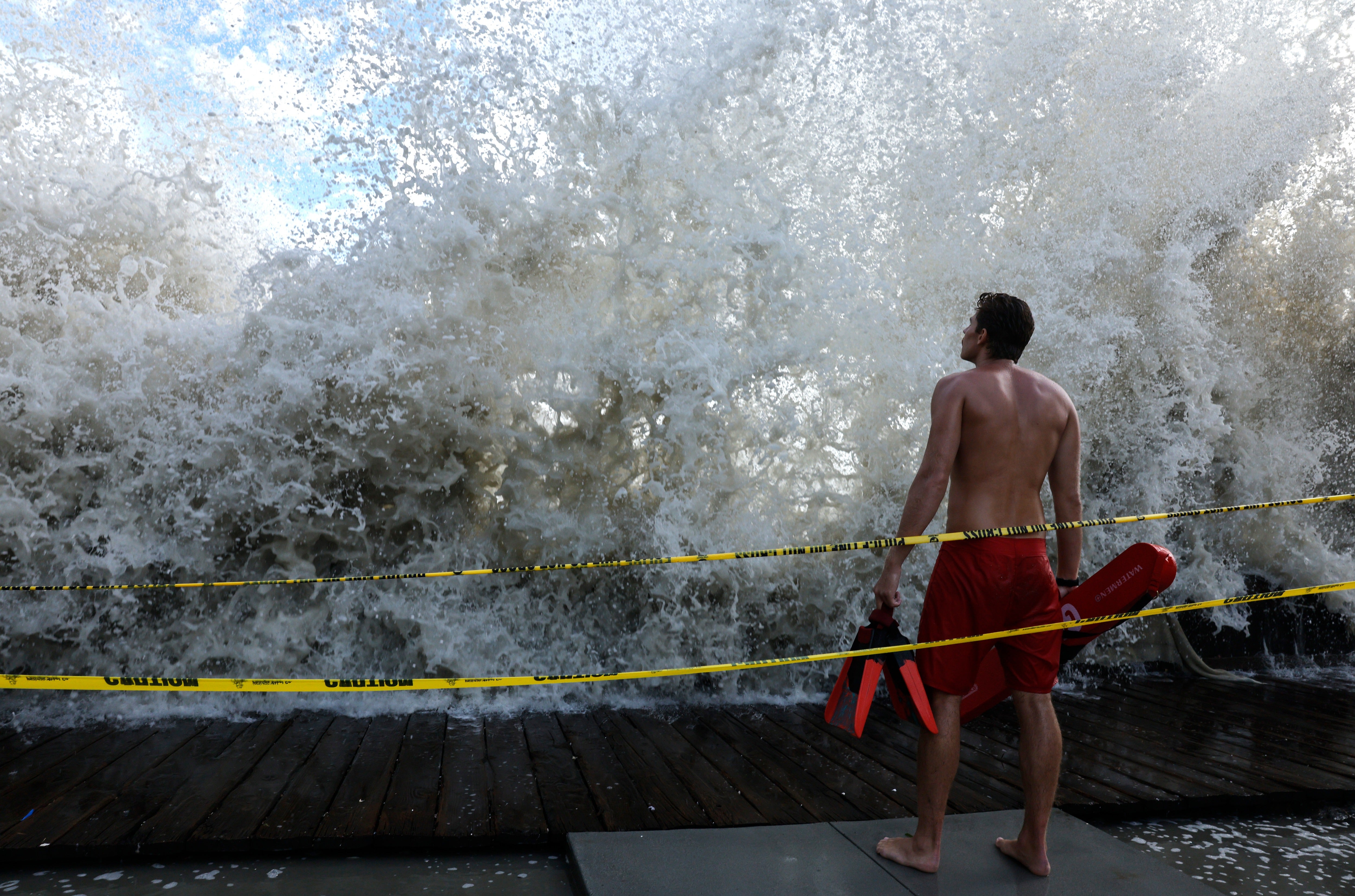 A lifeguard keeps watch along a closed boardwalk as a Pacific Ocean wave crashes over a seawall protecting homes on September 7, 2026 in Long Beach