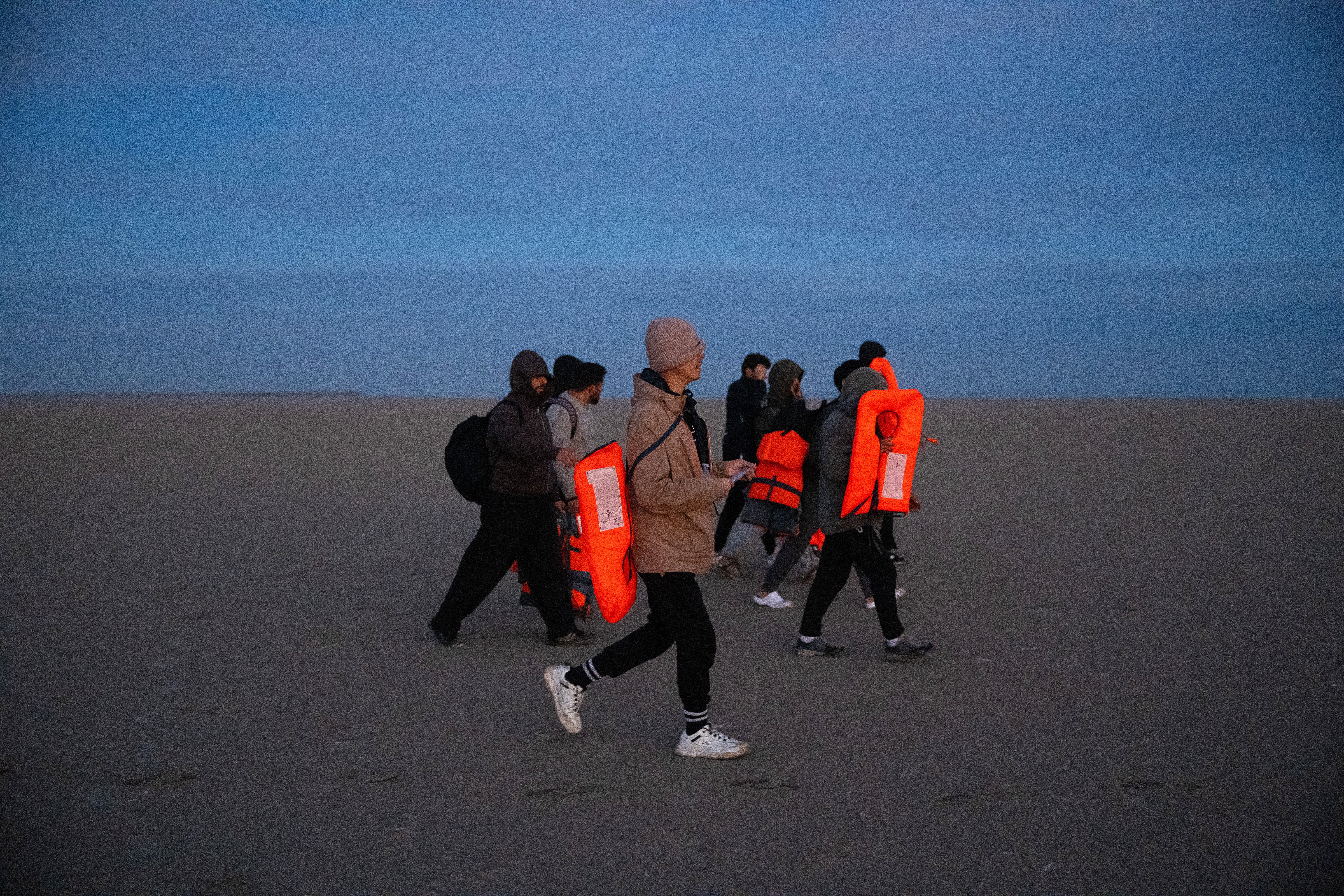 Migrants walk on the beach as they wait for a dinghy to sail into the English Channel on 23 September in Gravelines, France (Getty)