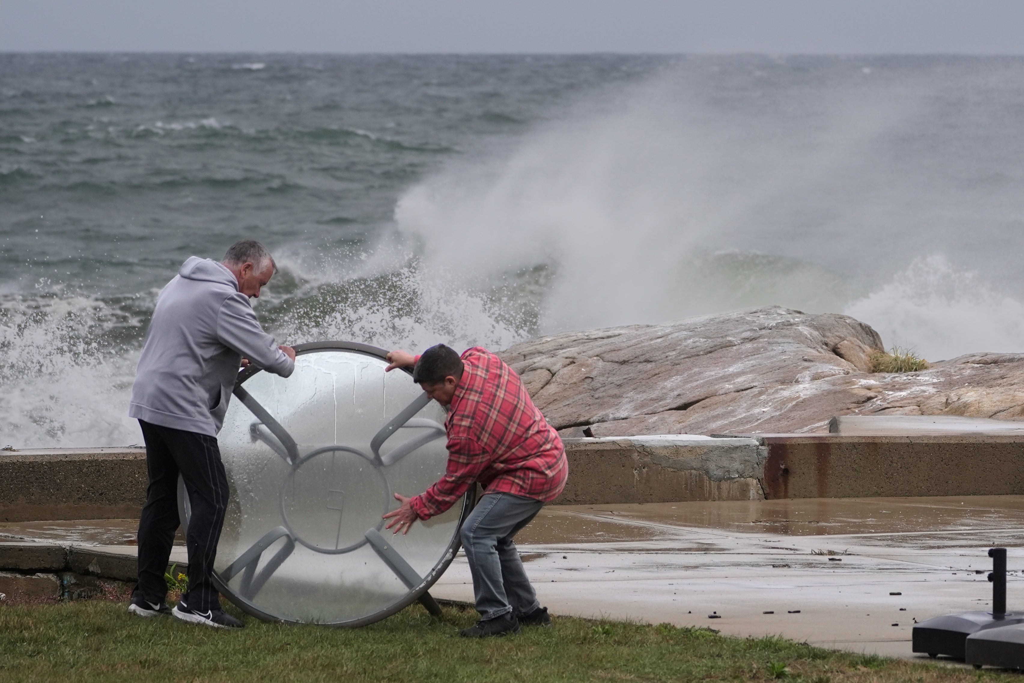 John Garrisi, left, and Gaige Graf move an outdoor table away from the shorefront during the early stages of the nor'easter storm on Friday in Gloucester, Mass. Impacts from the nor’easter are expected into next week