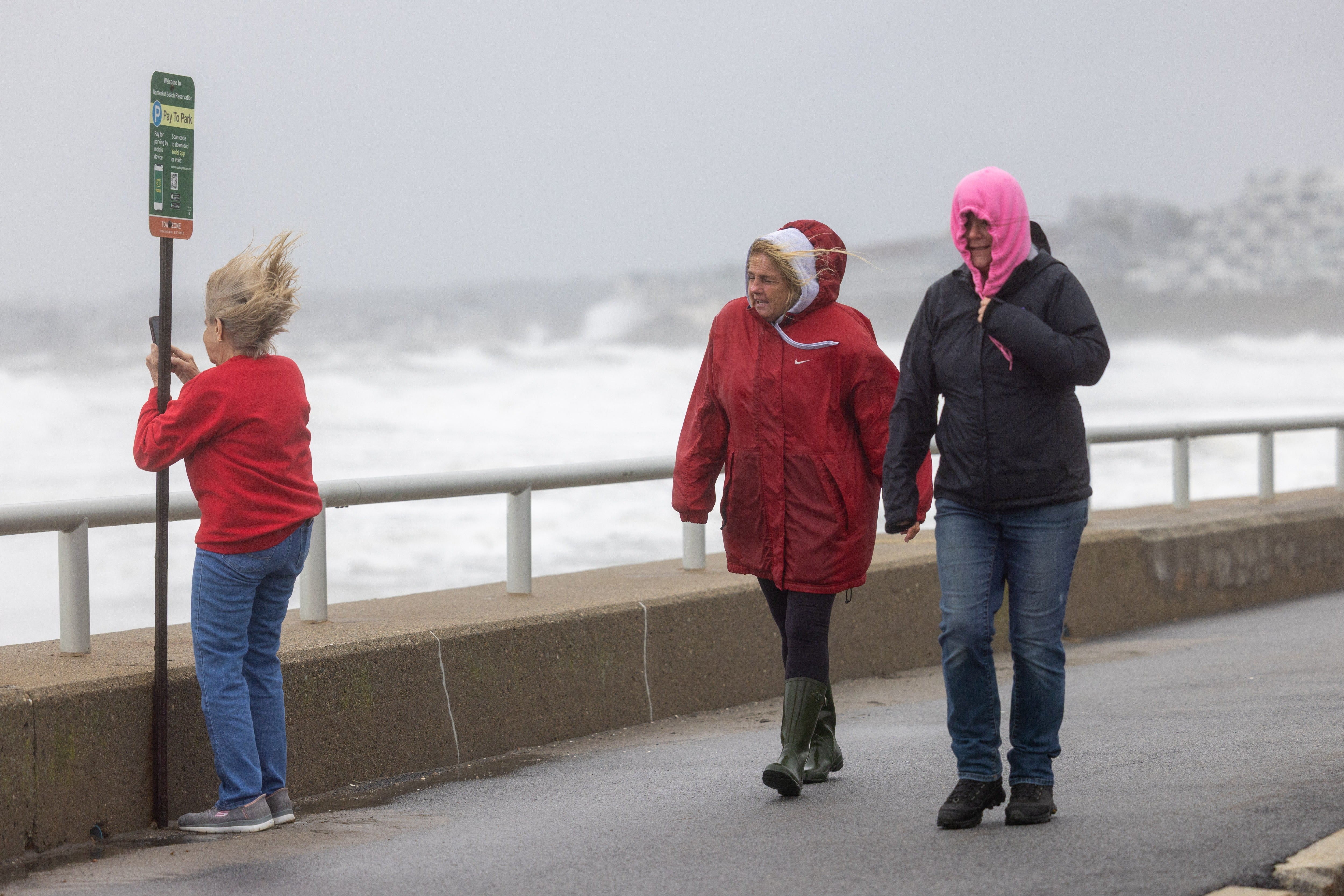 People walk along Nantasket Beach as a woman takes photos of high surf during high winds as a nor'easter bears down on September 26, 2026 in Hull, Massachusetts
