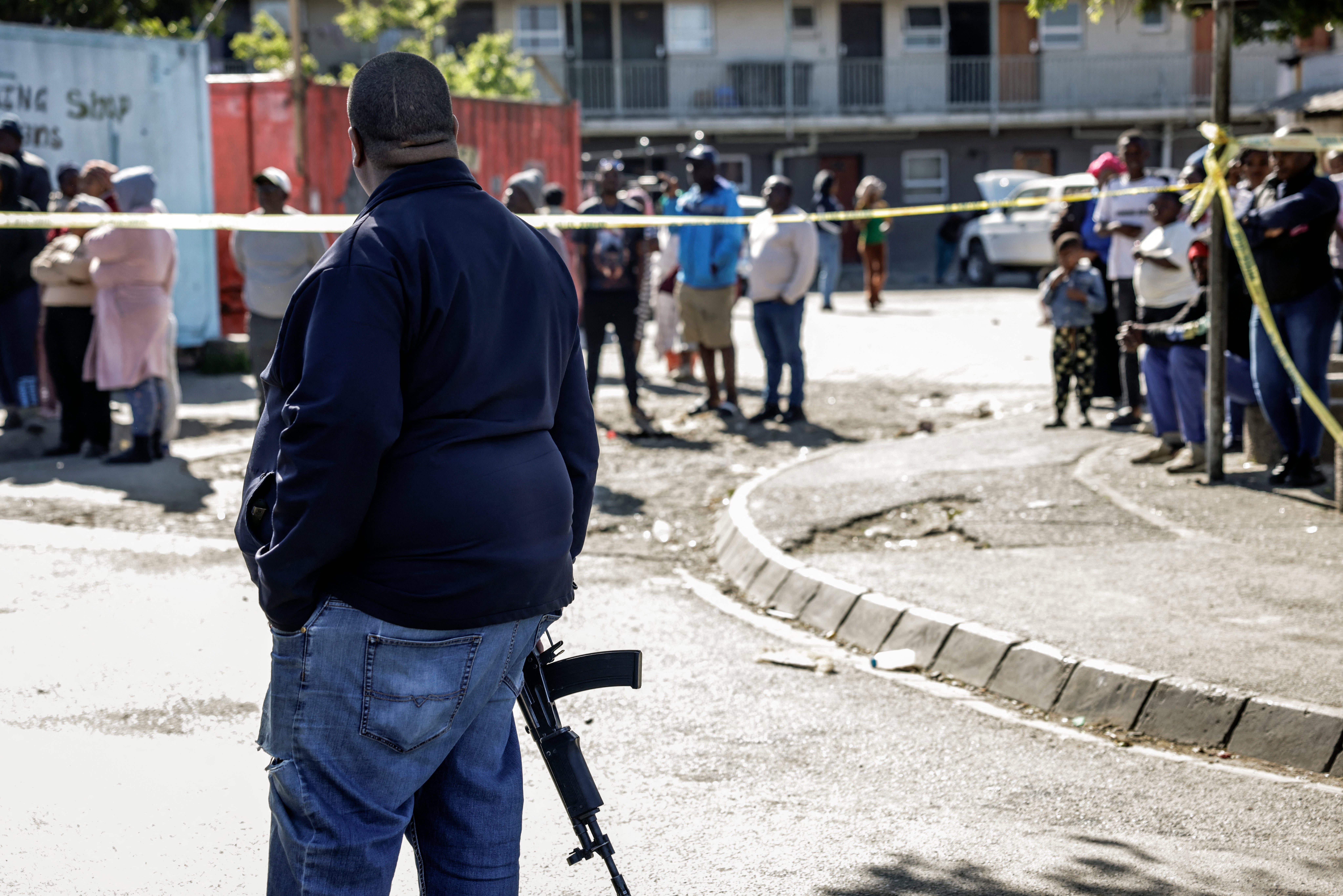 A member of the South African Police Service (SAPS) stands guard as bystanders look on behind police tape near an entertainment venue in Somerset West on September 27, 2026, after gunmen stormed the premises