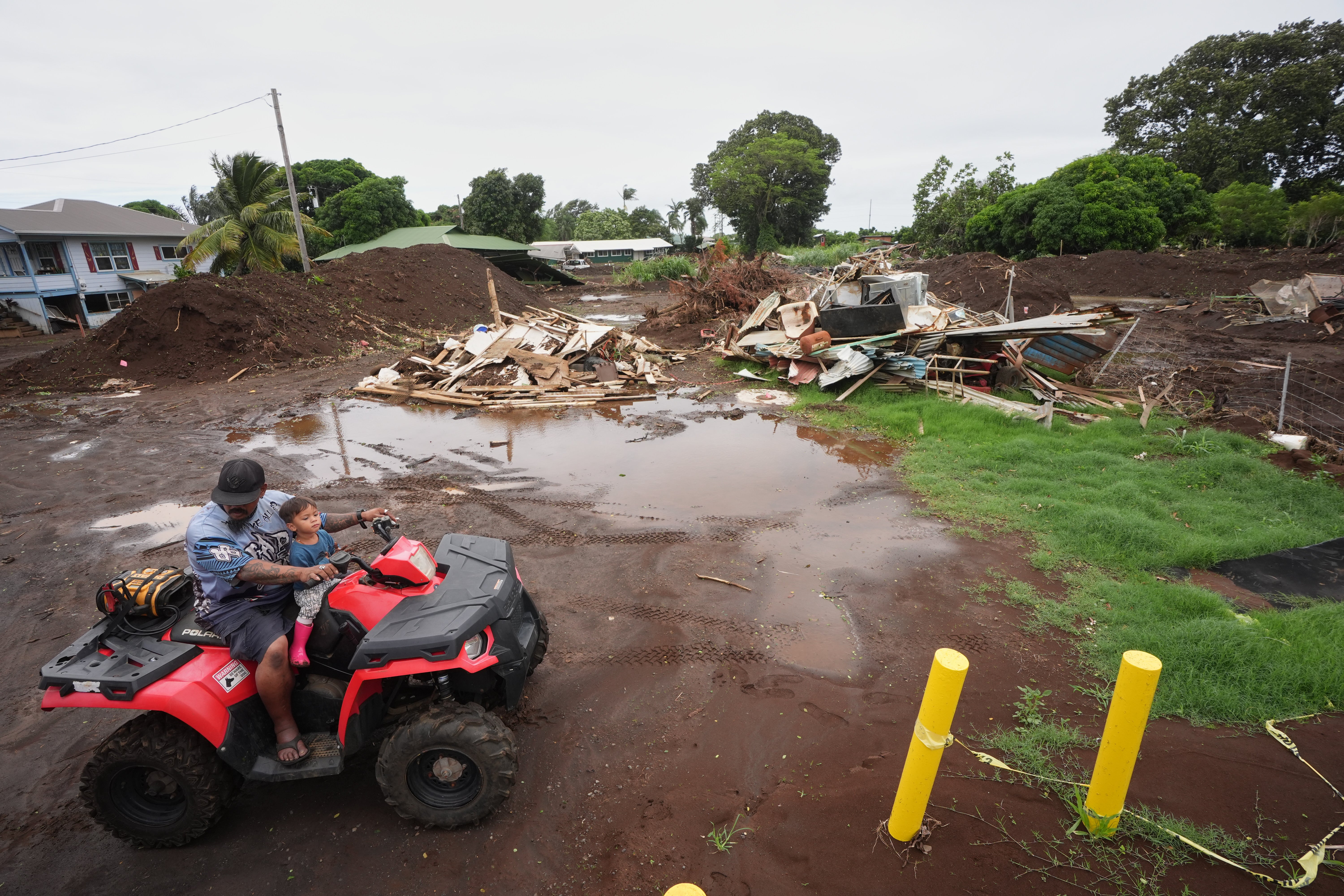 A man rides with his son near where a home was destroyed during last month's Hurricane Lala, as floodwaters from Hurricane Nolo recedes Sunday, Sept. 27, 2026, in Naalehu, Hawaii