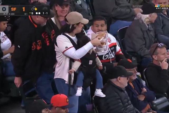 A woman named Erika carries her baby and trays of food back to her husband, Ramses, during a San Francisco Giants home game against the Minnesota Twins.