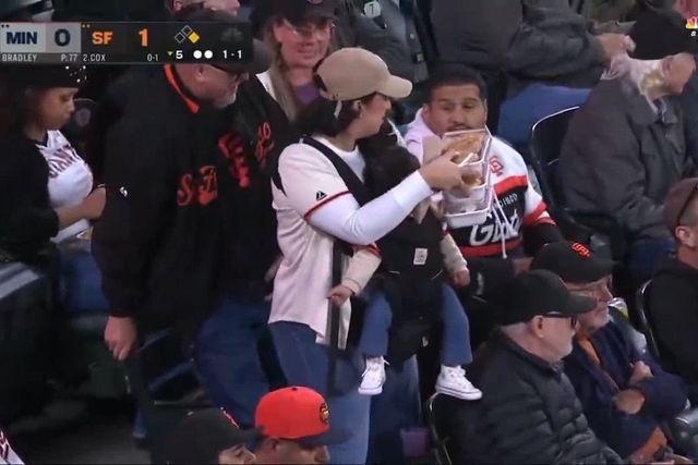 Una mujer llamada Erika lleva a su bebé y bandejas de comida de regreso a su esposo, Ramsés, durante un partido en casa de los Gigantes de San Francisco contra los Mellizos de Minnesota.