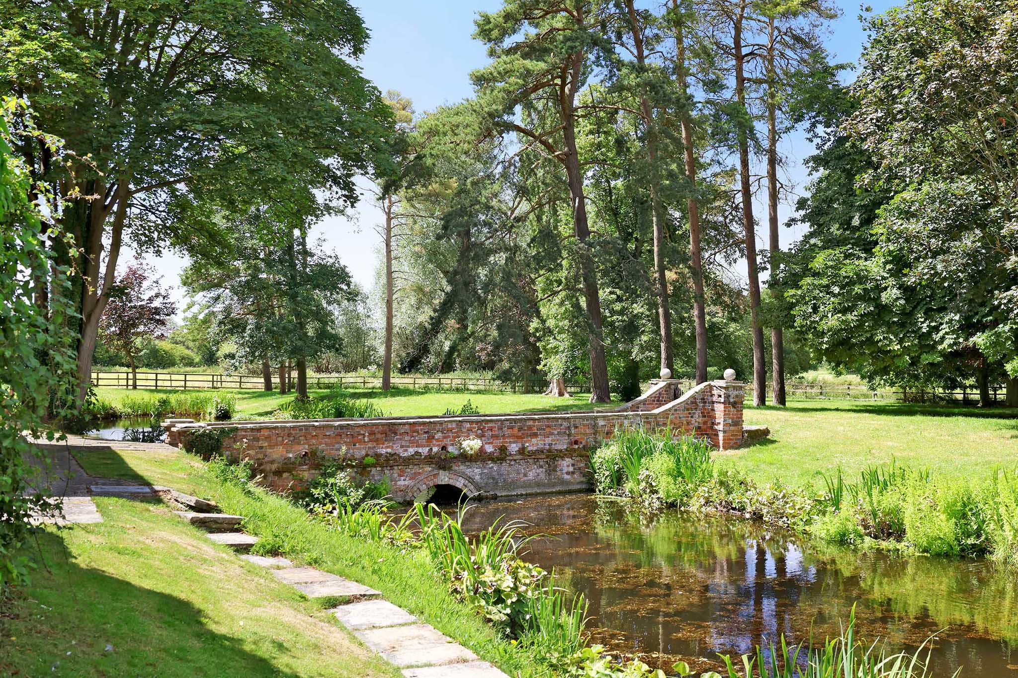 The house is surrounded by gardens with mature trees including a cherry and apple orchard, lawns and a charming moat