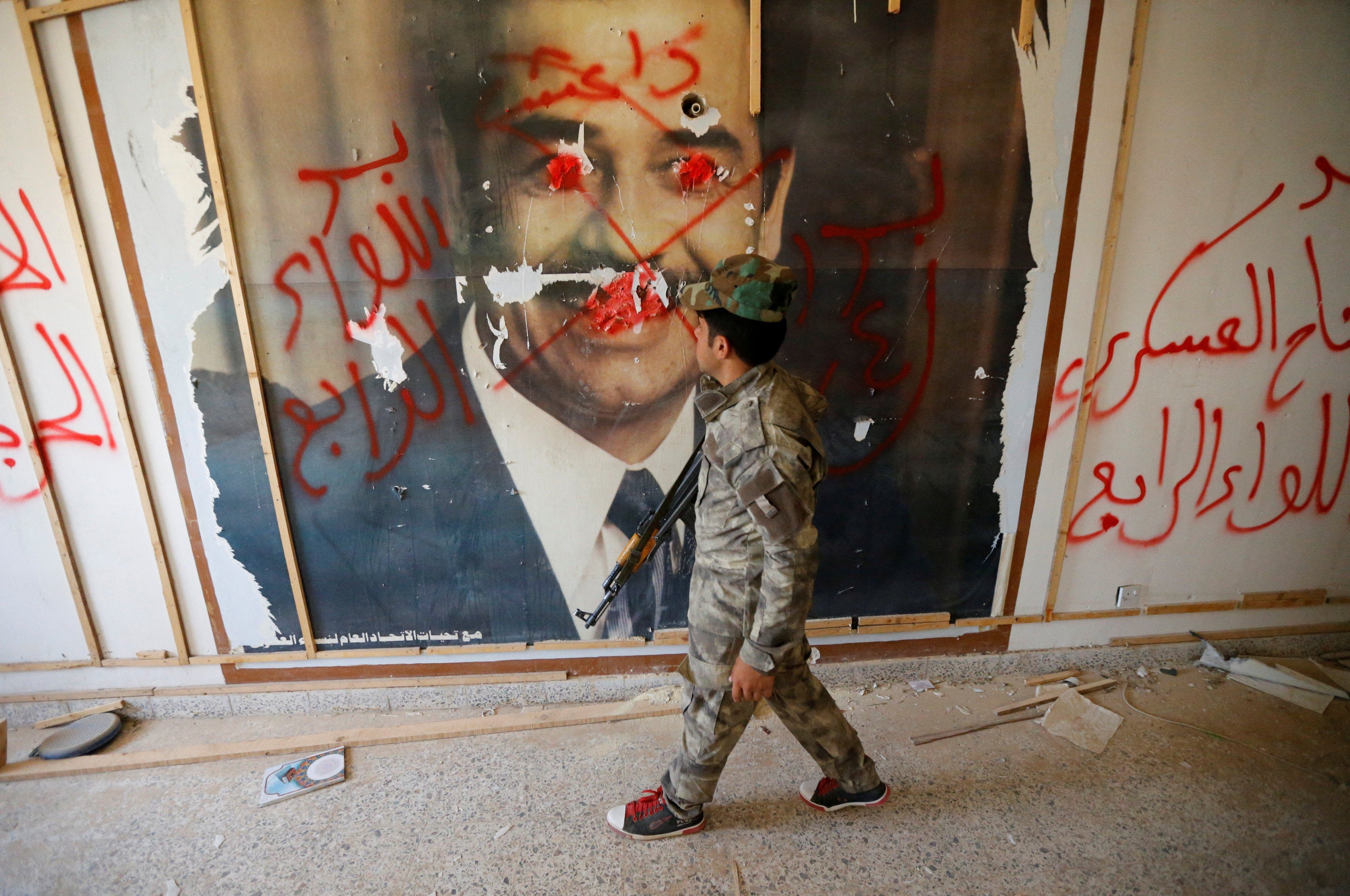 A fighter from the Iraqi Shi'ite Badr Organization looks at a poster depicting an image of former Iraqi President Saddam Hussein