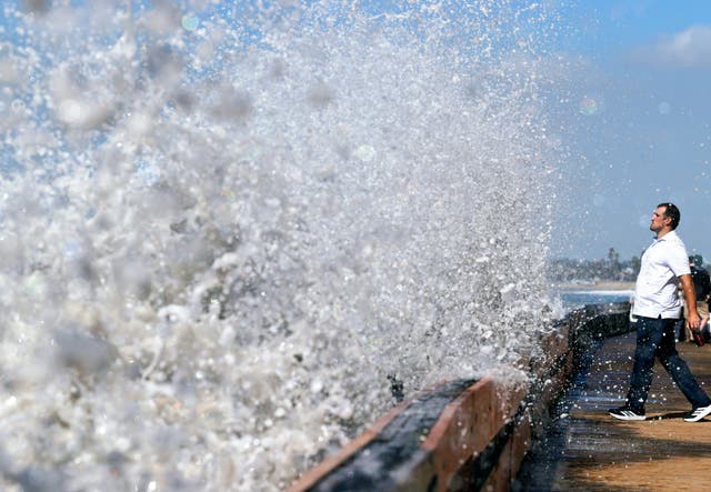 A person watches as a Pacific Ocean wave crashes into a seawall protecting beachfront homes in Long Beach, California, on Monday. The remnants of Pacific Hurricane Polo are bringing widespread flooding threats through the weekend