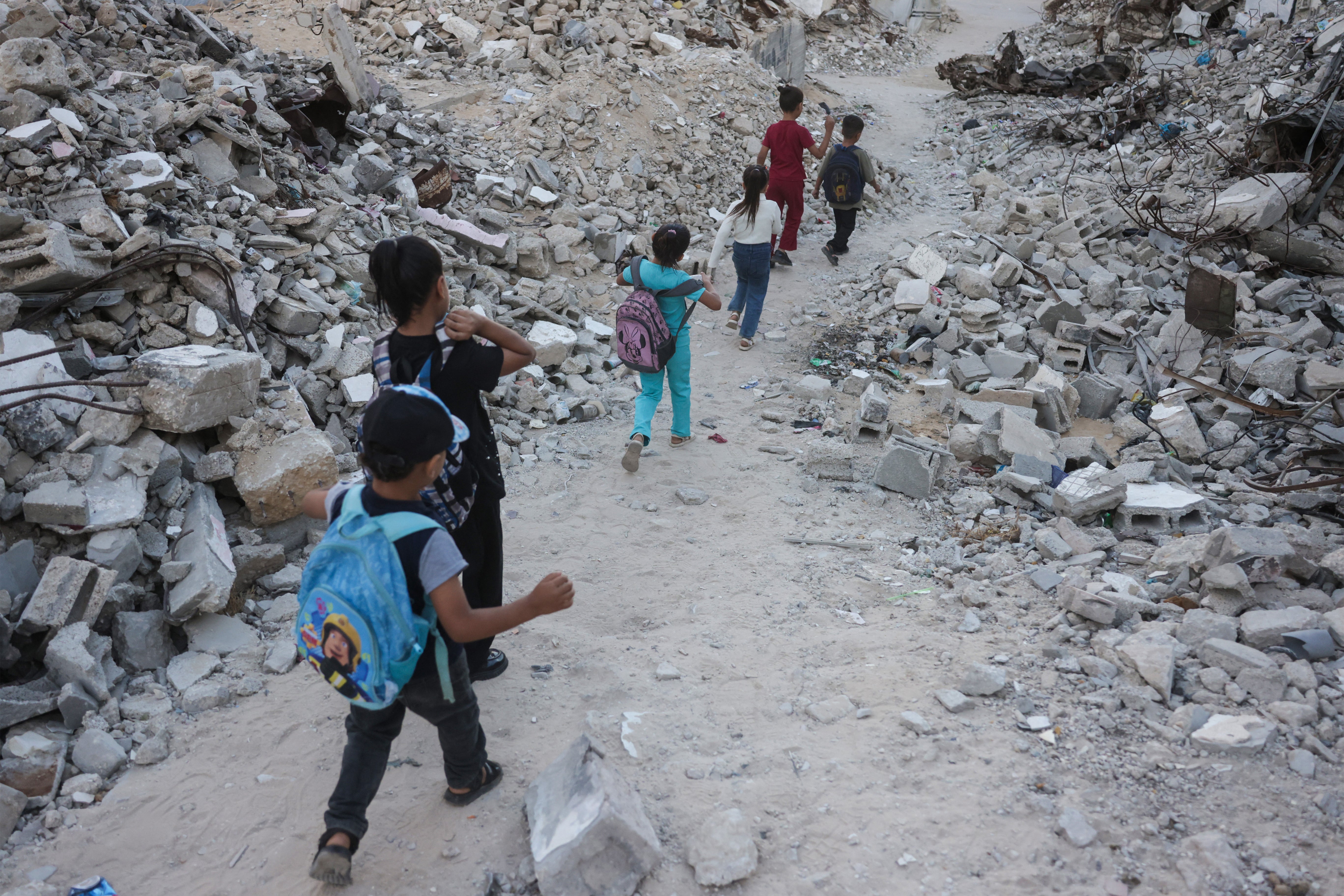 Palestinian children walk to school amid the rubble of destroyed buildings as the academic year begins in Khan Yunis