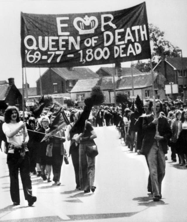 Members of the Provisional Irish Republican Army (IRA) hold a banner reading "Elizabeth Regina, Queen of Death, 69-77-1,800 dead" march 10 August 1977 in the streets of Belfast