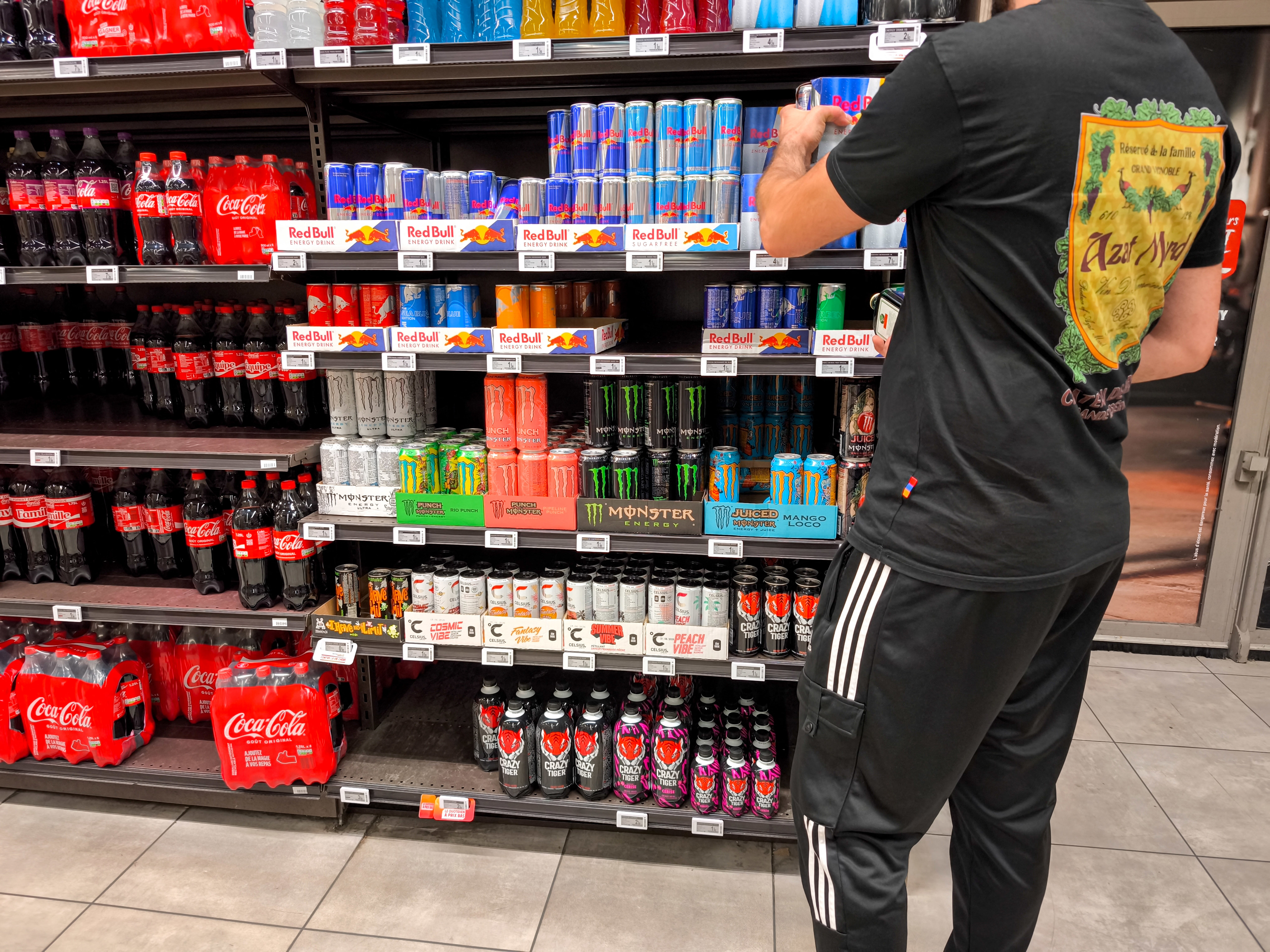 A man stands in front of the shelves of a section of iron cans of energy drinks sweetened with taurine from the brands Redbull, Monster and Celsius and grabs a package in an InterMarche supermarket in Valence, France, on September 7, 2025