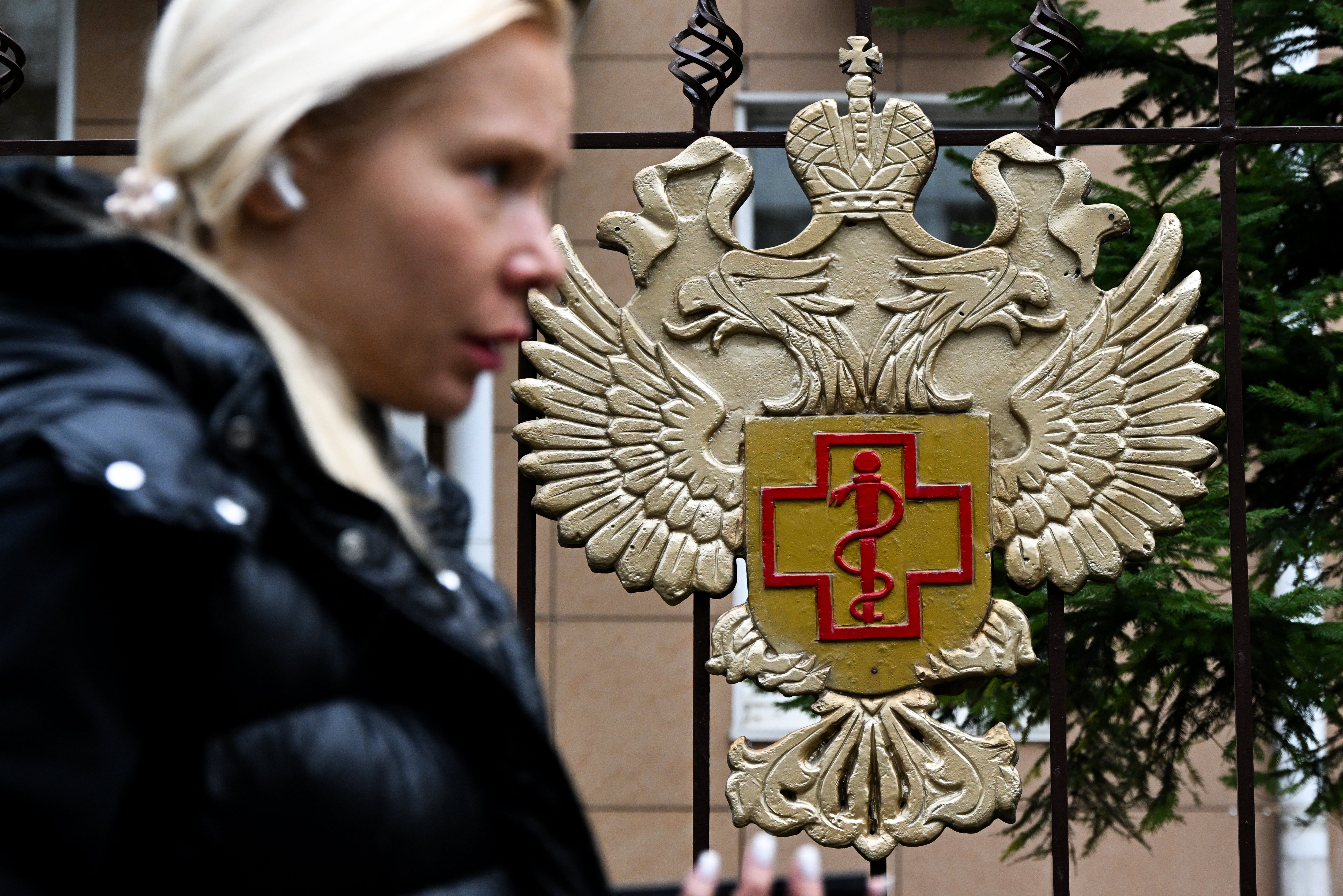 A woman walks past the logo of Russia's consumer and health watchdog Rospotrebnadzor sitting on its grounds' fencing in Moscow