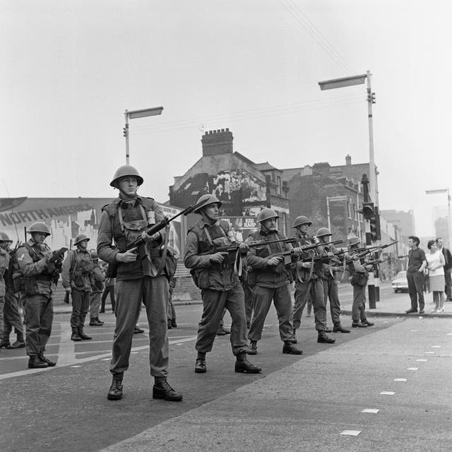 A line of British troops stands guard in the Falls Road area of riot-torn Belfast