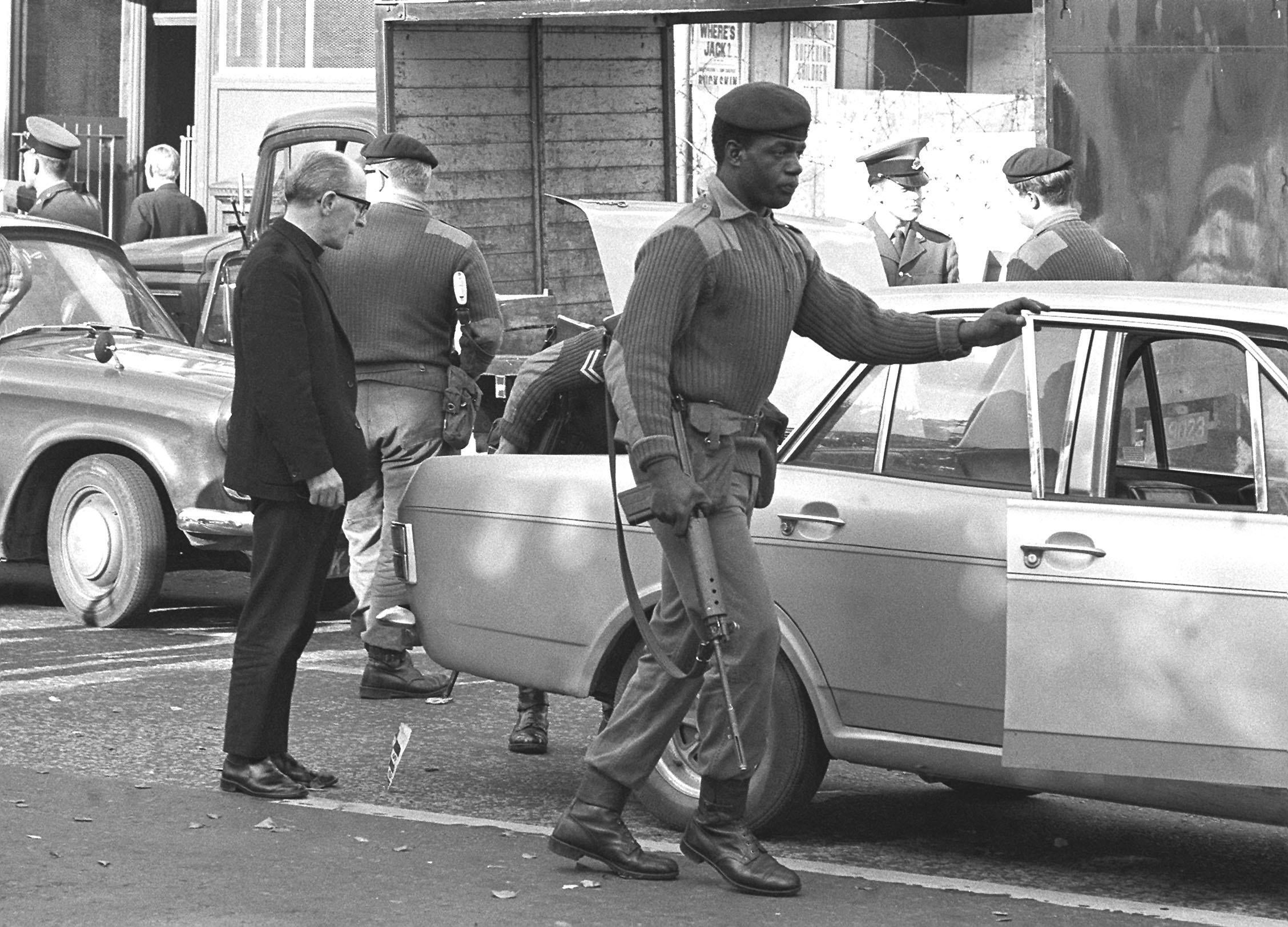 A priest stands by as his car is searched by troops in the Falls Road area, during the extra security precautions taken in Belfast