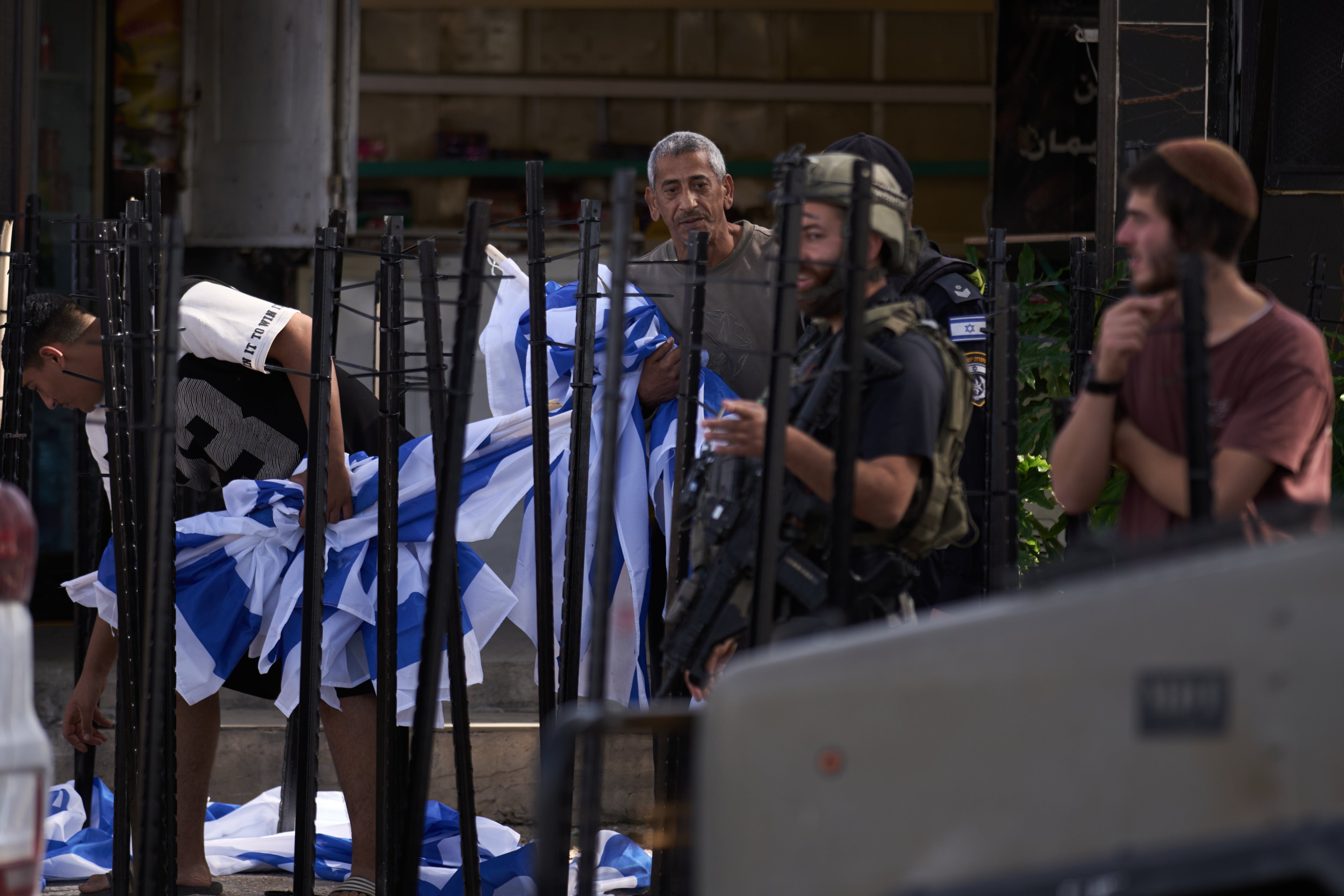 Palestinian Mouayad Oweis carries Israeli flags after dozens of other flags were set up by setllers blocking access to his shop in the West Bank village of al-Lubban al-Sharqiya, Thursday, Oct. 8, 2026. (AP Photo/Leo Correa)