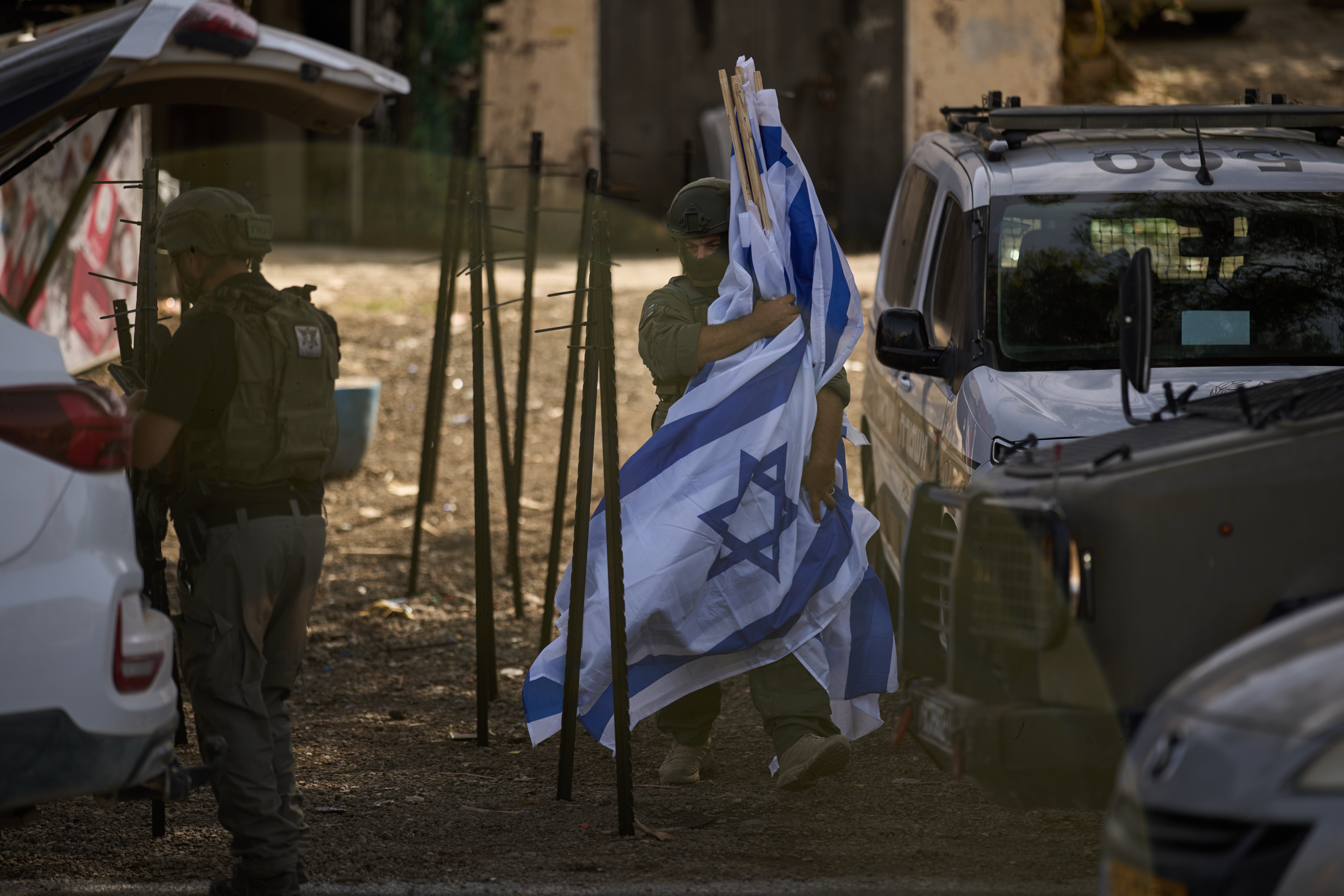 A member of Israeli forces carries flags after dozens of other Israeli flags were set up in front of a shop belonging to Palestinian Mouayad Oweis, blocking access to his business in the West Bank village of al-Lubban al-Sharqiya, Thursday, Oct. 8, 2026. (AP Photo/Leo Correa)
