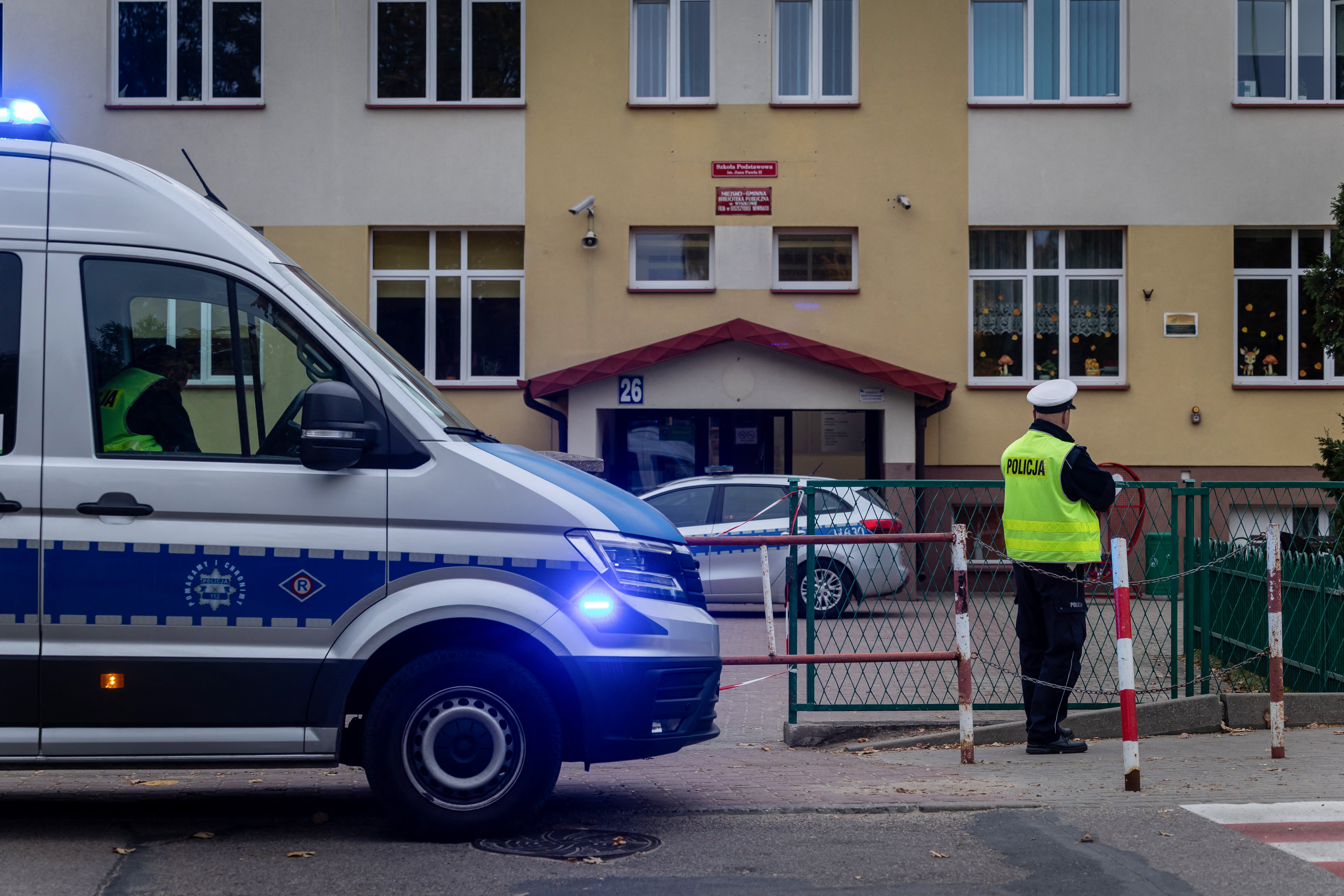 Police officers stand in front of a school in Poland where a 15-year-old fatally stabbed the caretaker of his former school