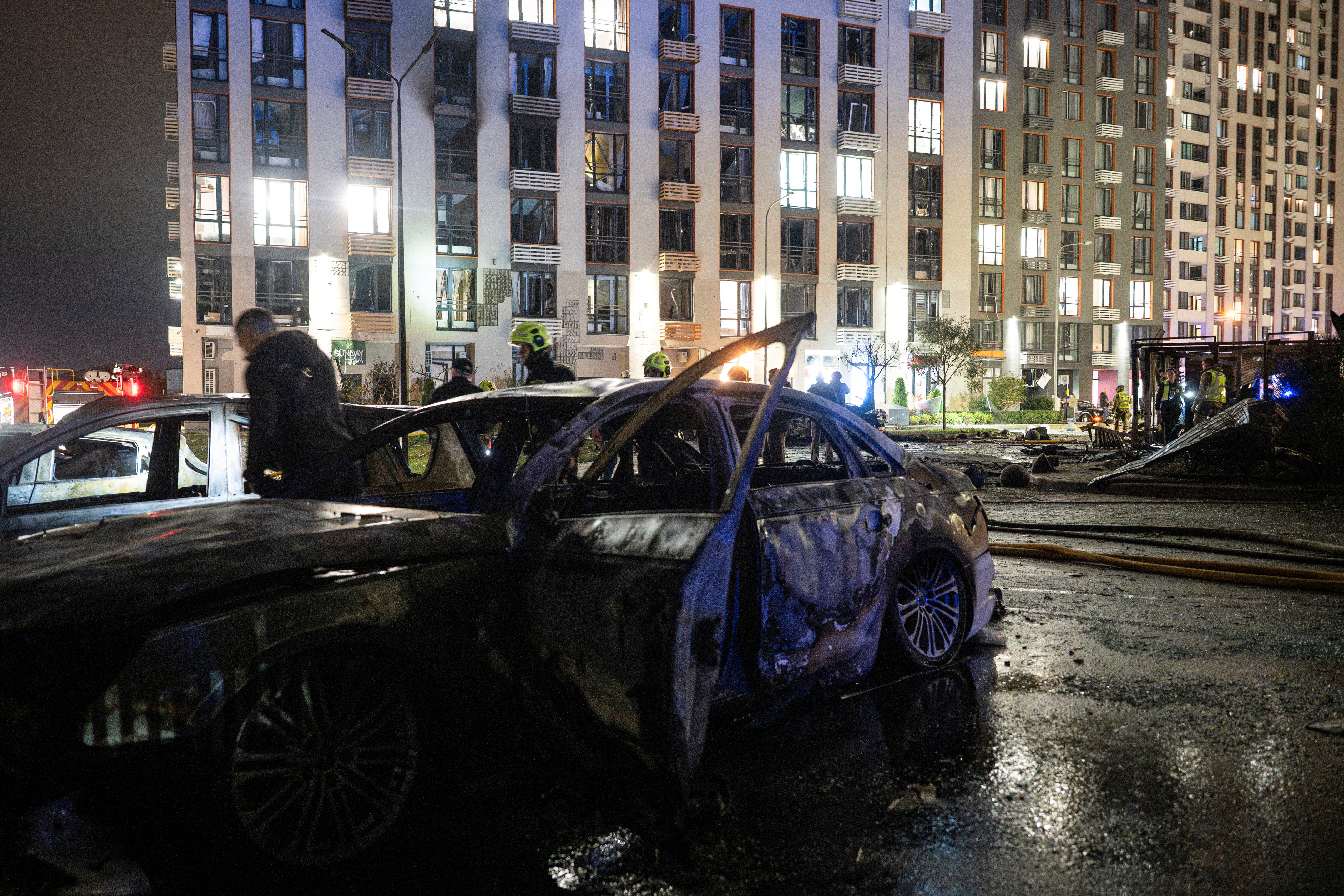 Ukrainian firefighters inspect burned vehicles in front of a high-rise residential building damaged following a Russian drone attack, in Kyiv