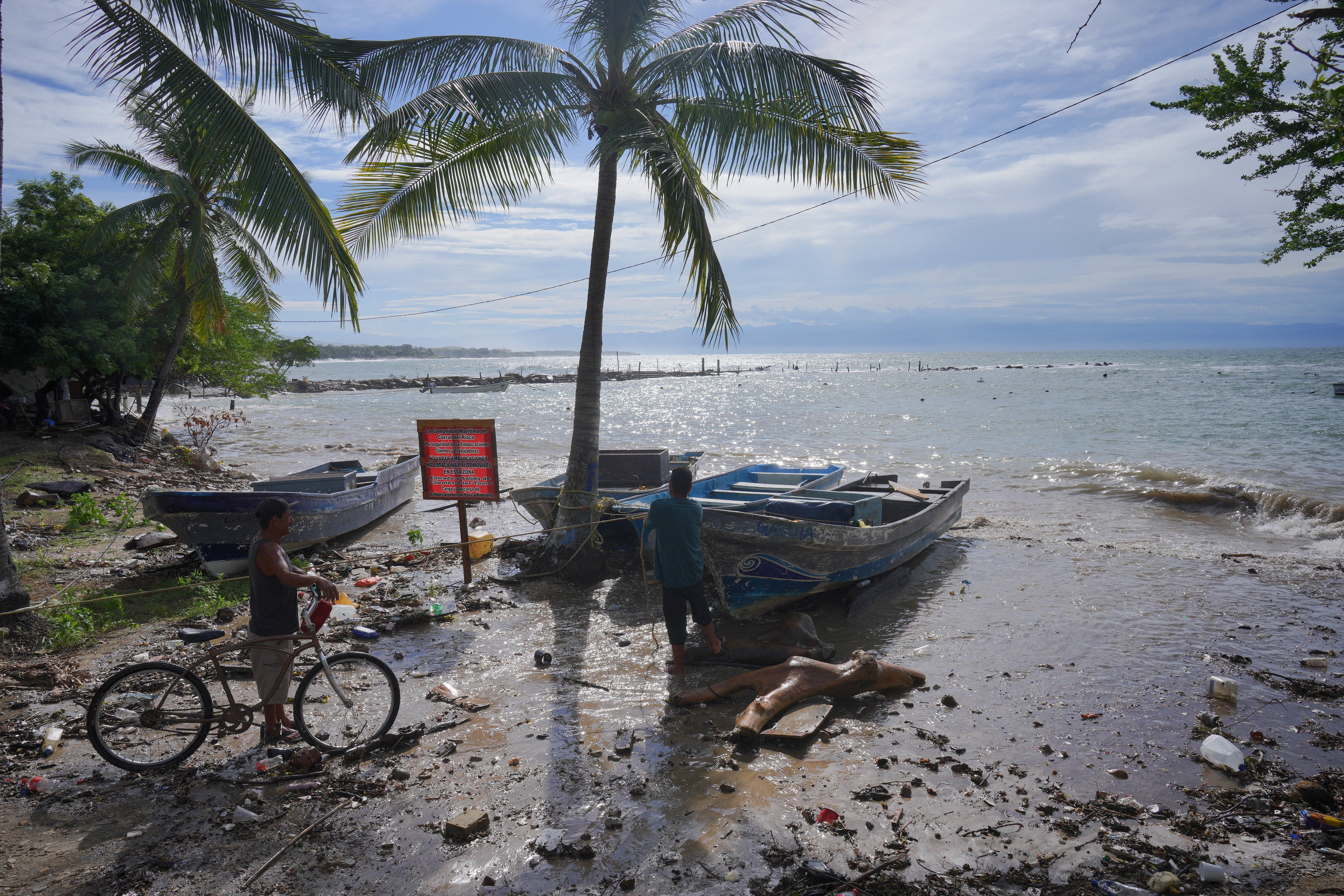 People stand next to fishing boats along the shoreline in Punta de Mita