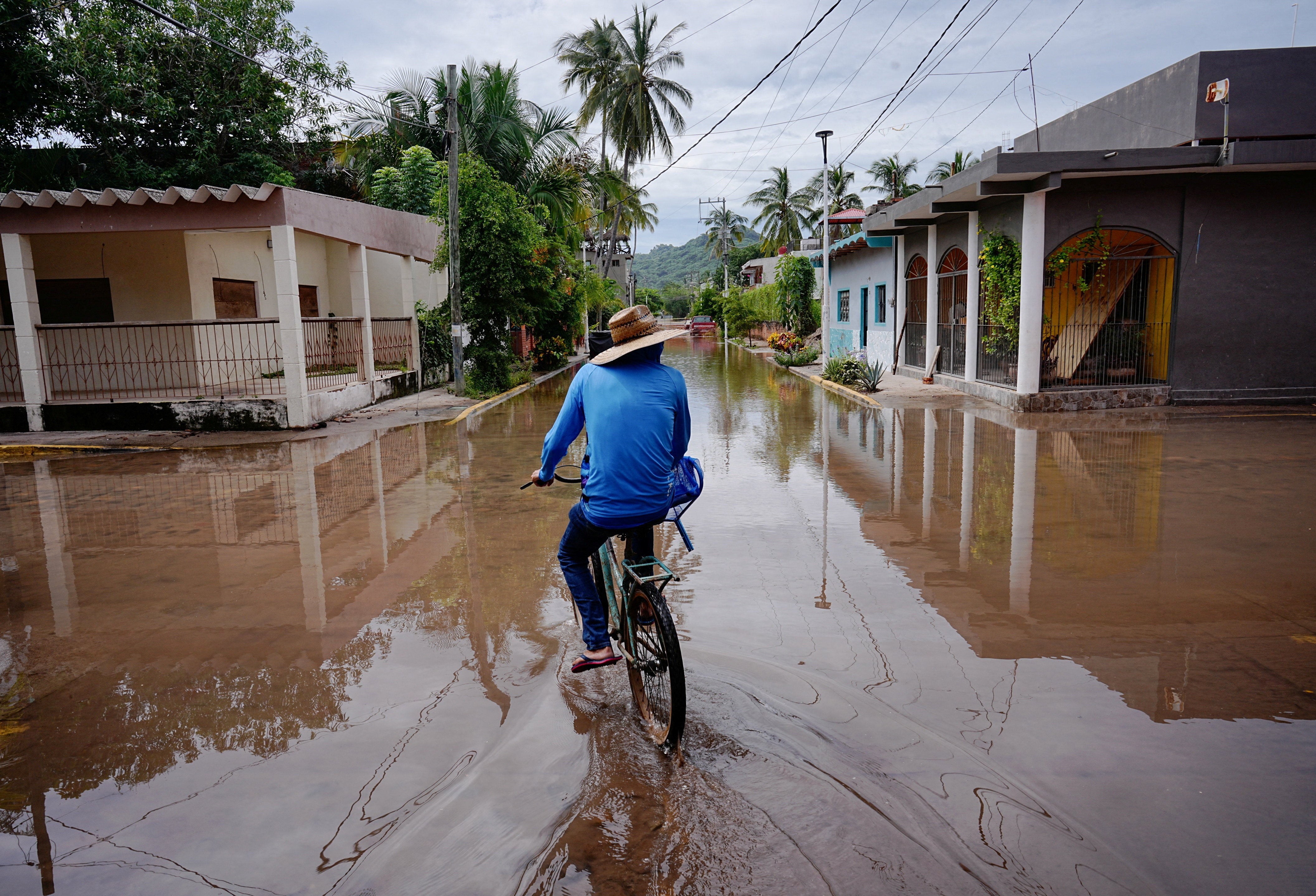 A person rides a bicycle through a flooded street as Hurricane Simon remains off Mexico's Pacific coast