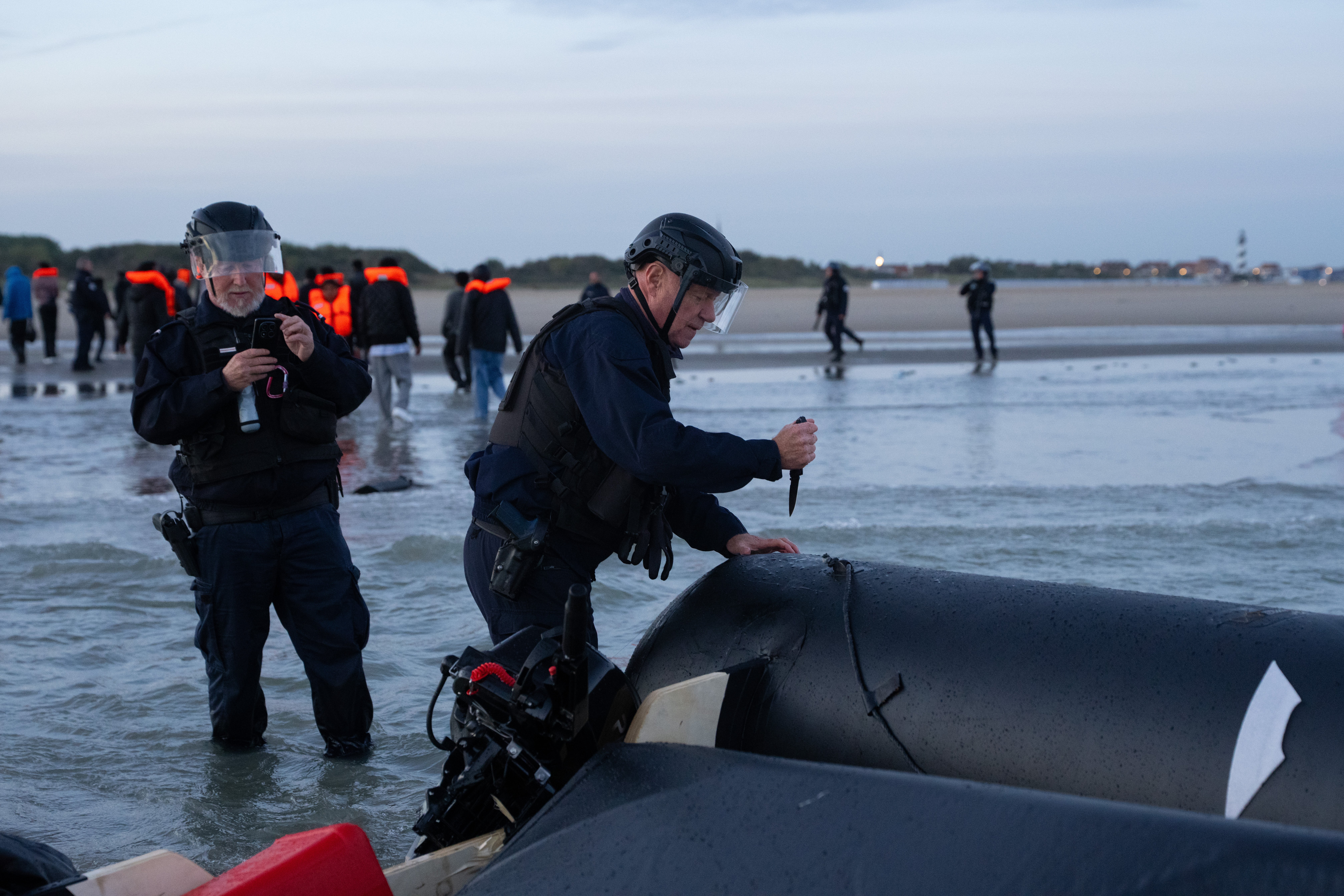 A police officer slashes a dinghy that was abandoned by migrants attempting to cross into the English Channel after the engine failed last month