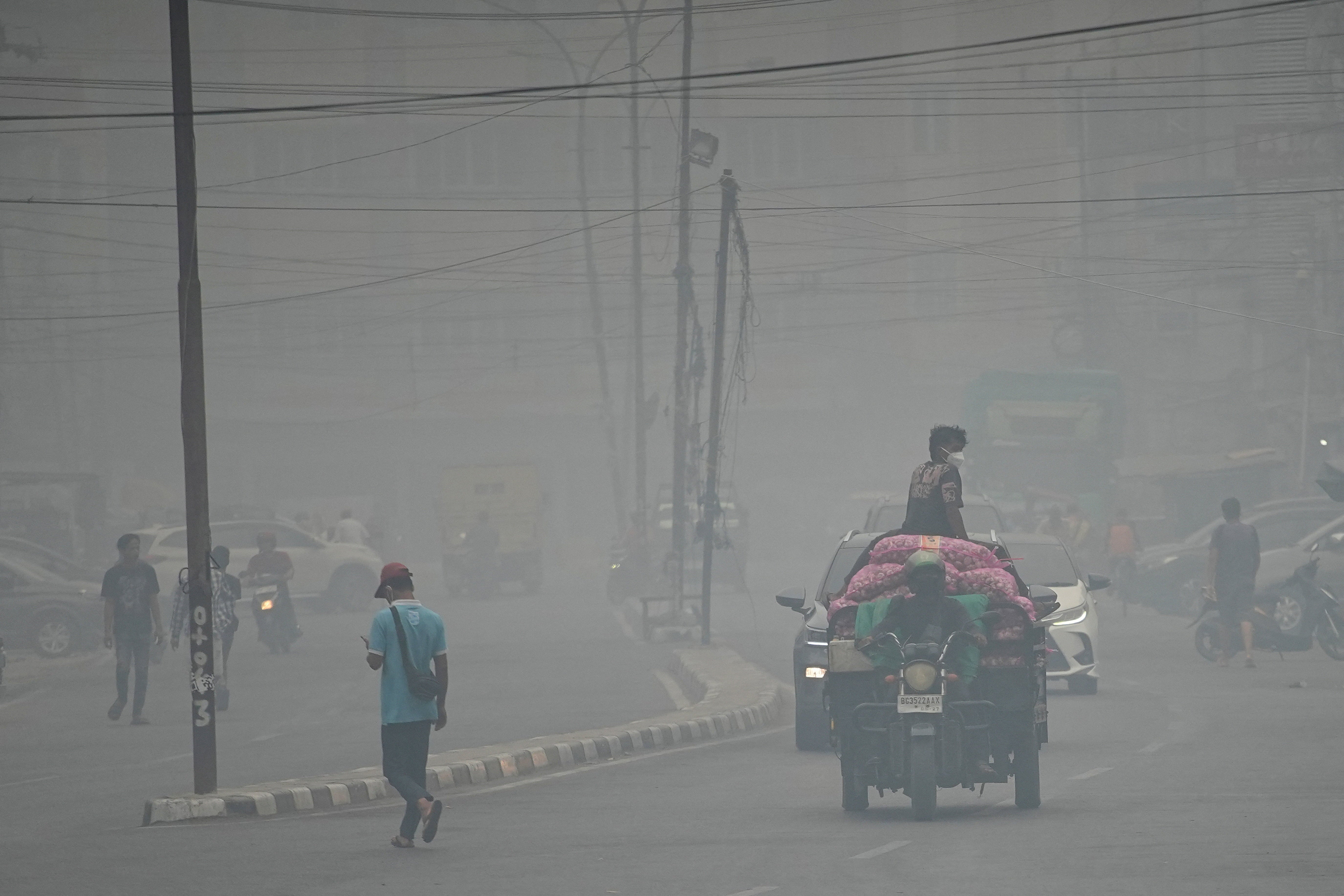 People wearing protective masks ride on a three-wheeled vehicle through a road as haze from wildfires shrouds the area in Palembang, South Sumatra province, Indonesia, October 15, 2026