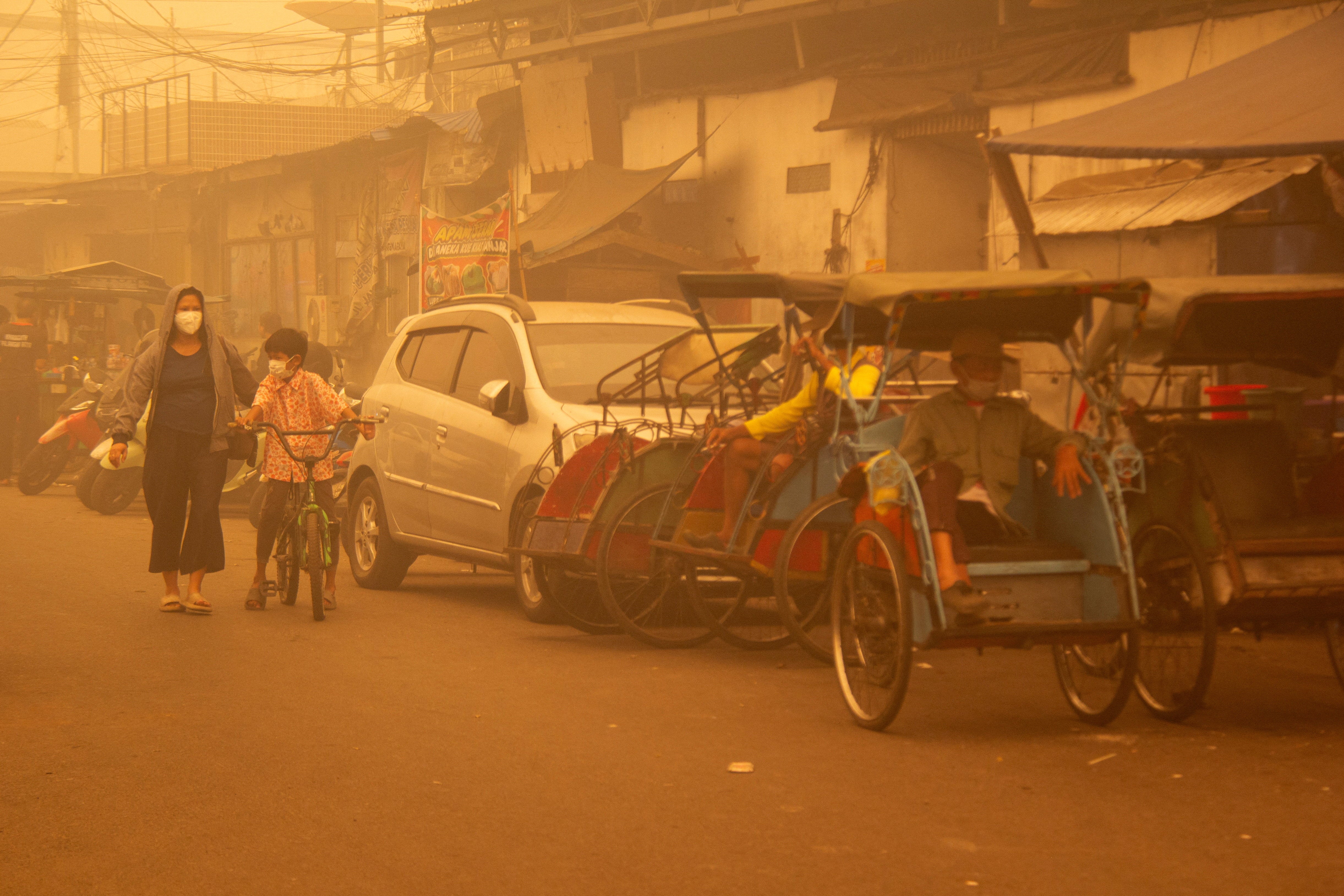 People wearing protective masks walk through the street as haze from wildfires shrouds the area in Palangka Raya, Central Kalimantan province, Indonesia, October 14, 2026