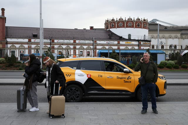 People stand next to a Yandex Taxi car on a street in Moscow, Russia, October 11