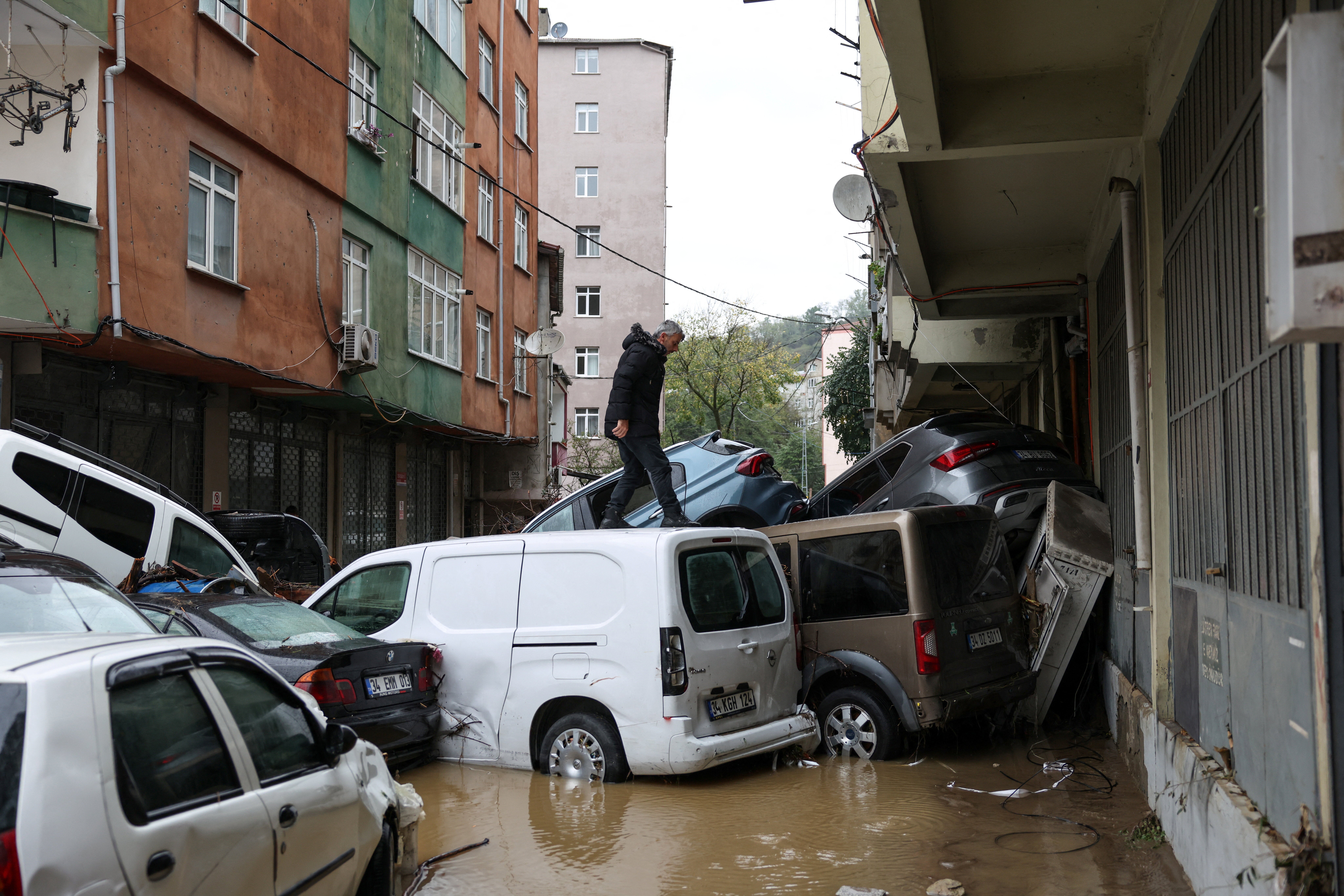 A man walks over damaged vehicles piled up in a flooded residential neighbourhood after heavy rains in Istanbul