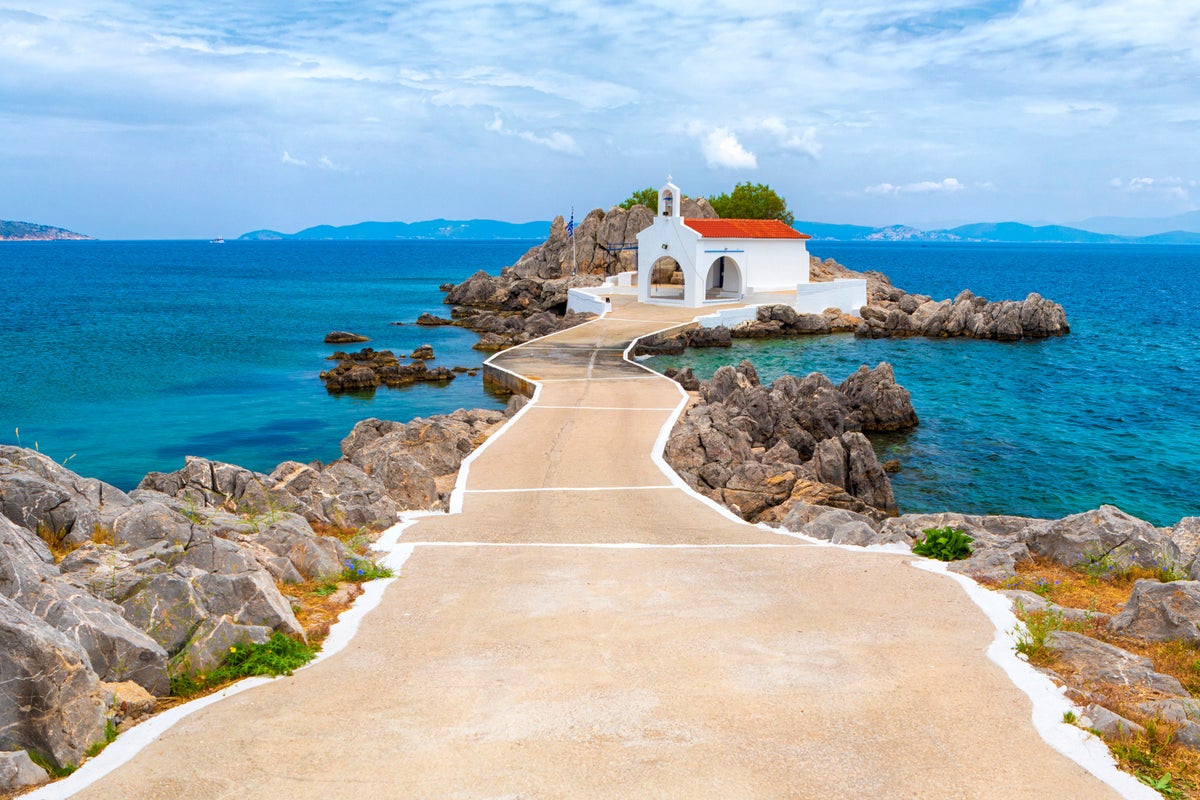 A small white church stands on a rocky outcrop by the sea