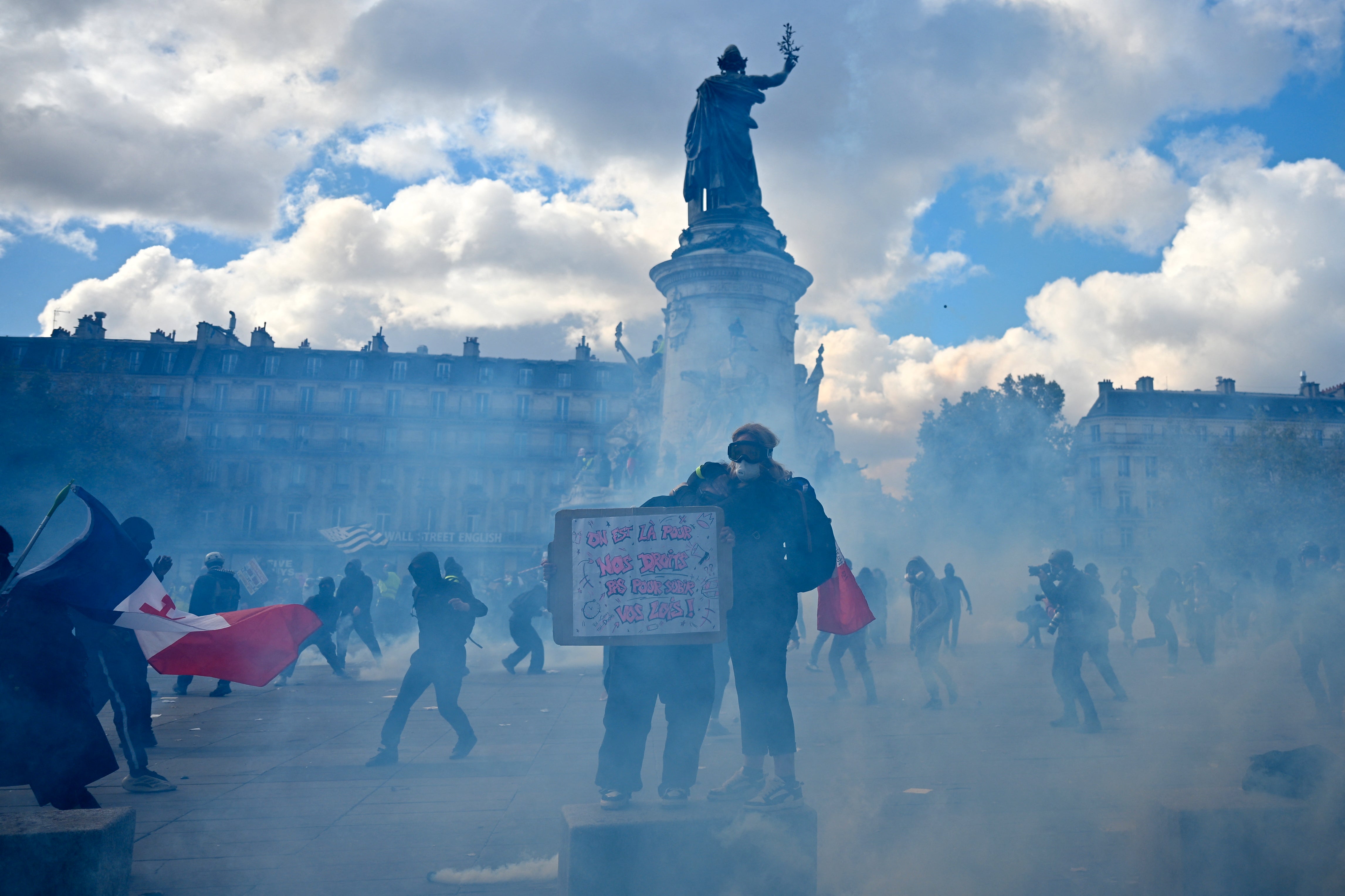 A protester holds a placard amid tear gas smoke as clashes erupt at Place de la Republique