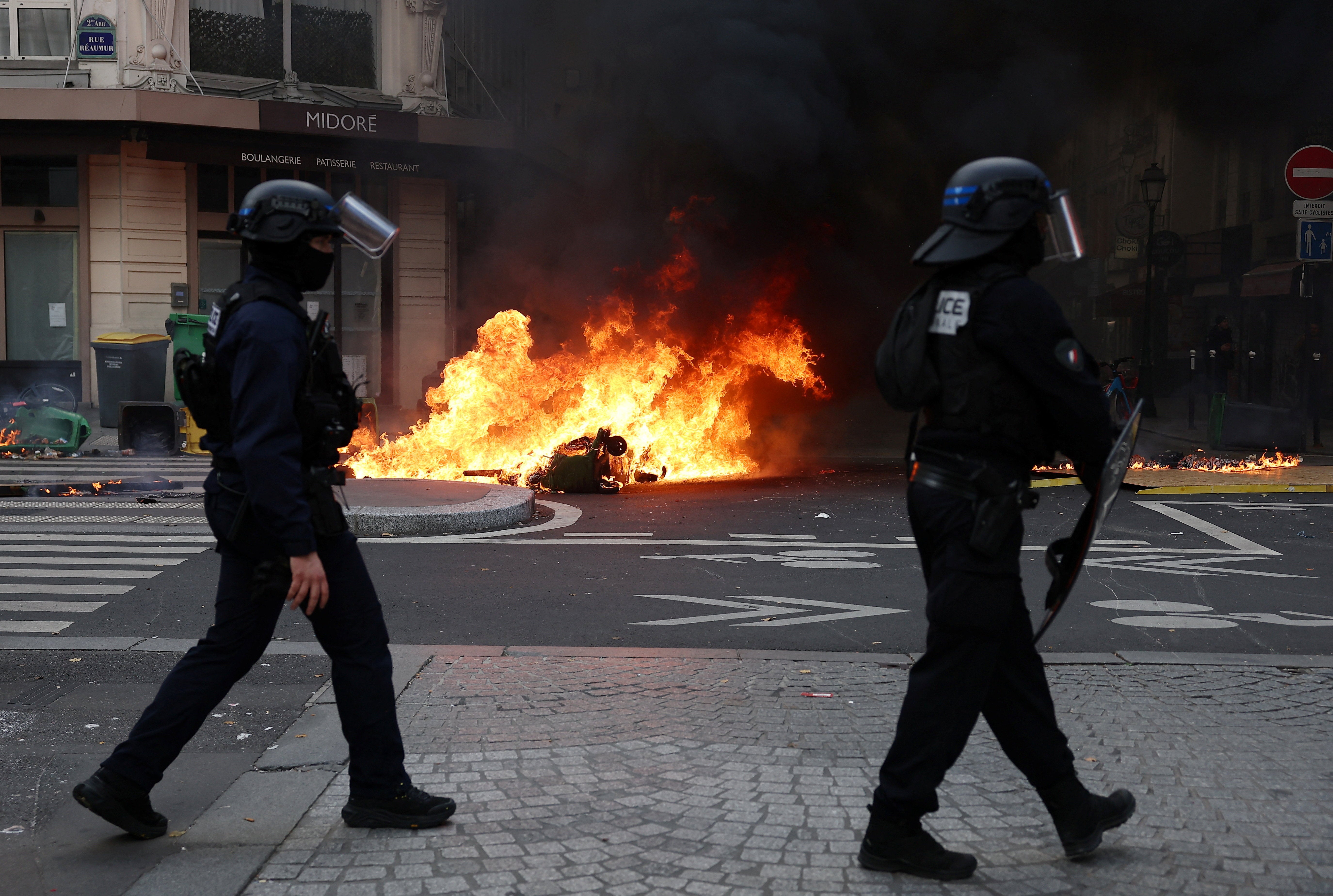 French riot police walk past burning objects in a street in Paris