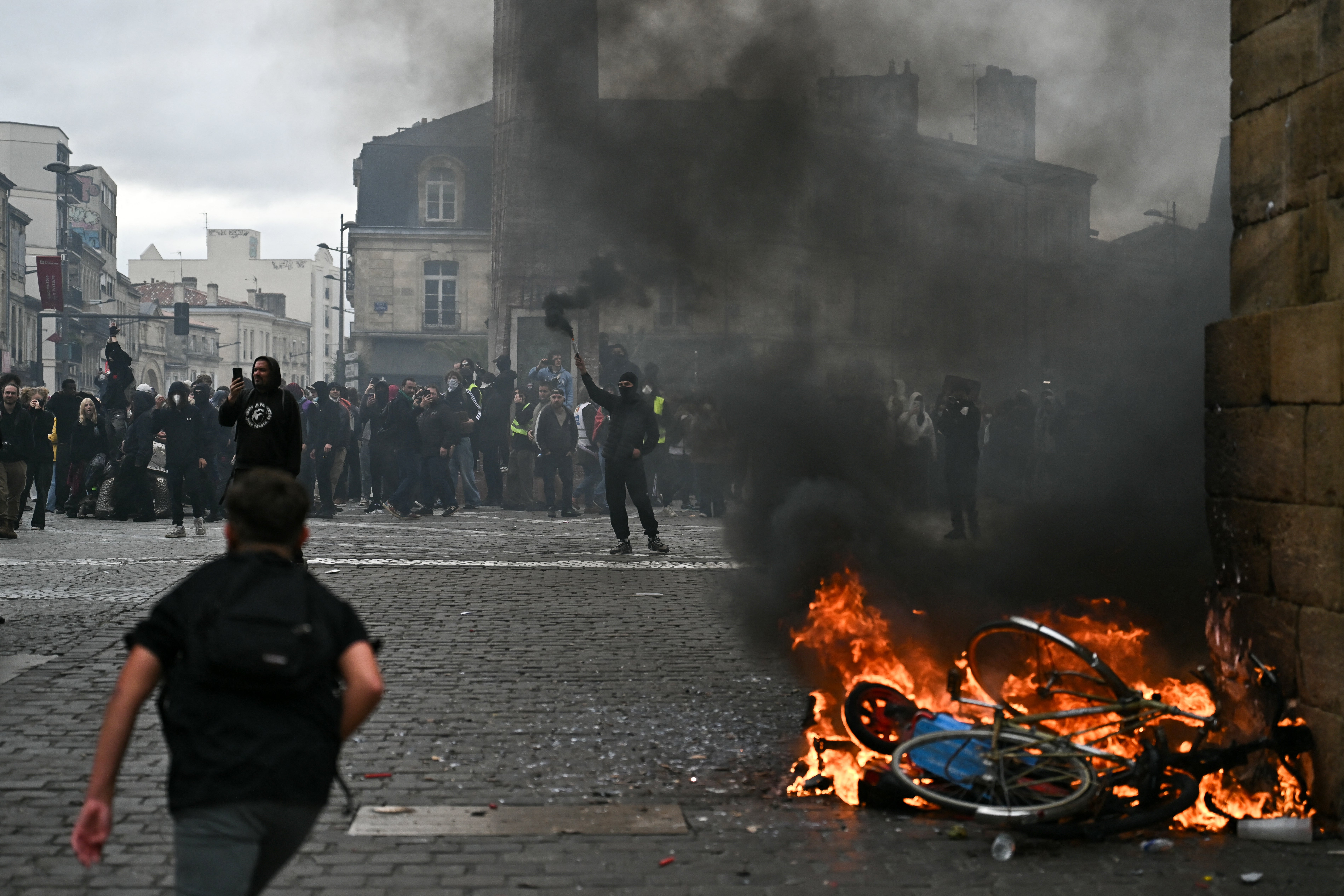 A protester lights smoke flares next to a fire during a demonstration to protest against the 'high cost of living'
