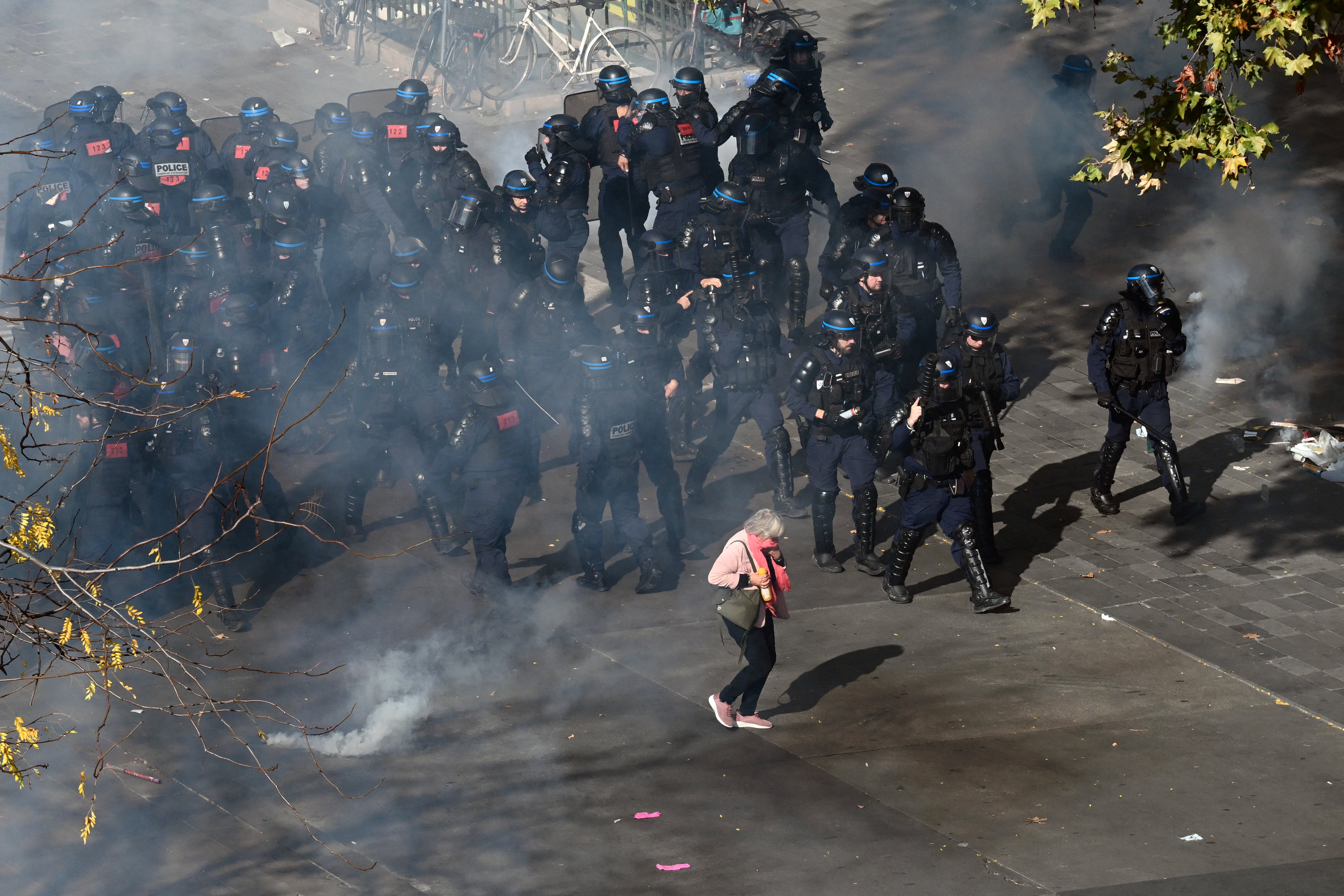 An elderly woman walks amid tear gas smoke past French police