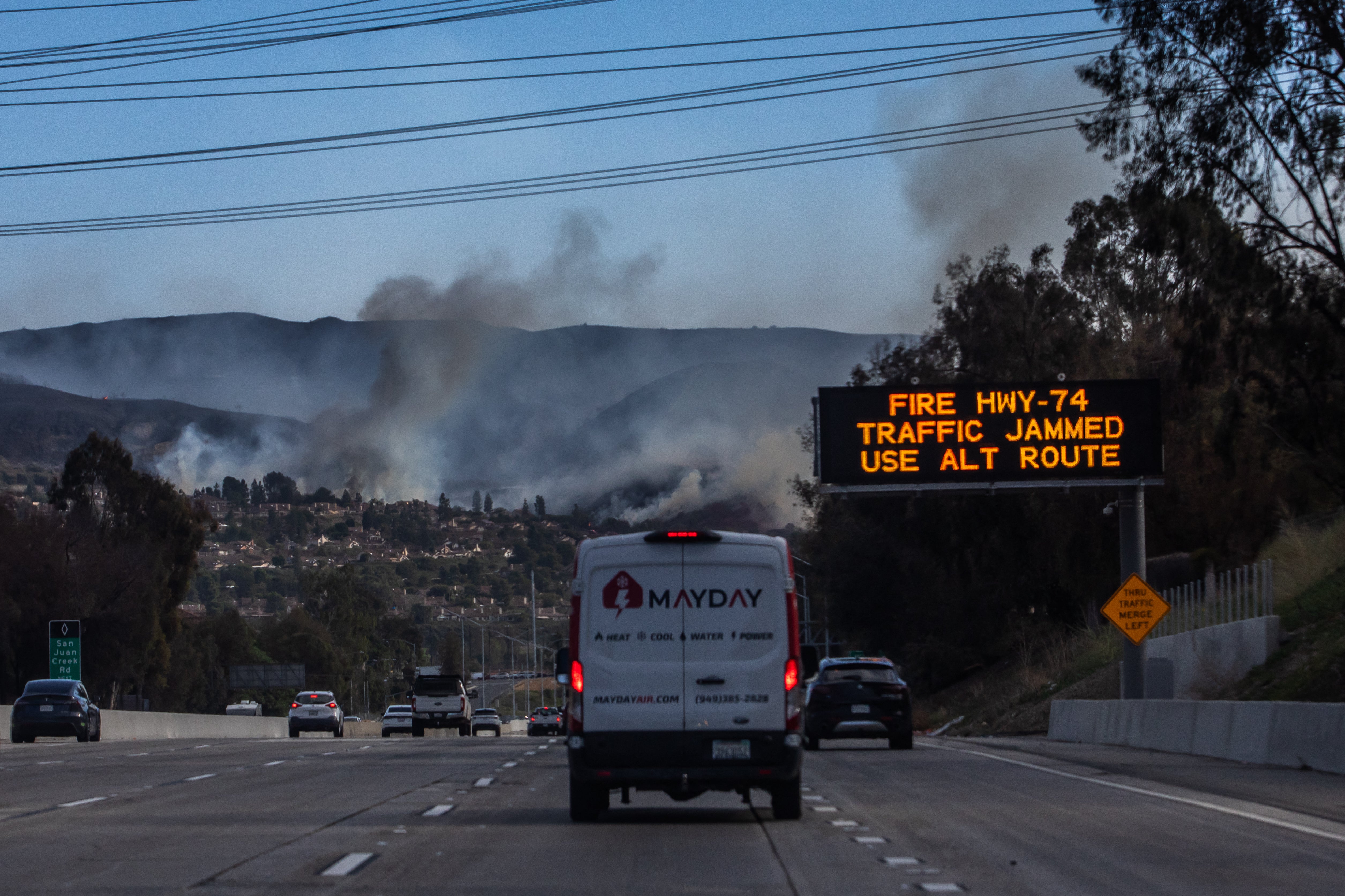 A traffic sign alerts motorists about the Norte Fire, seen in the background on the Interstate 5 freeway in San Juan Capistrano, California