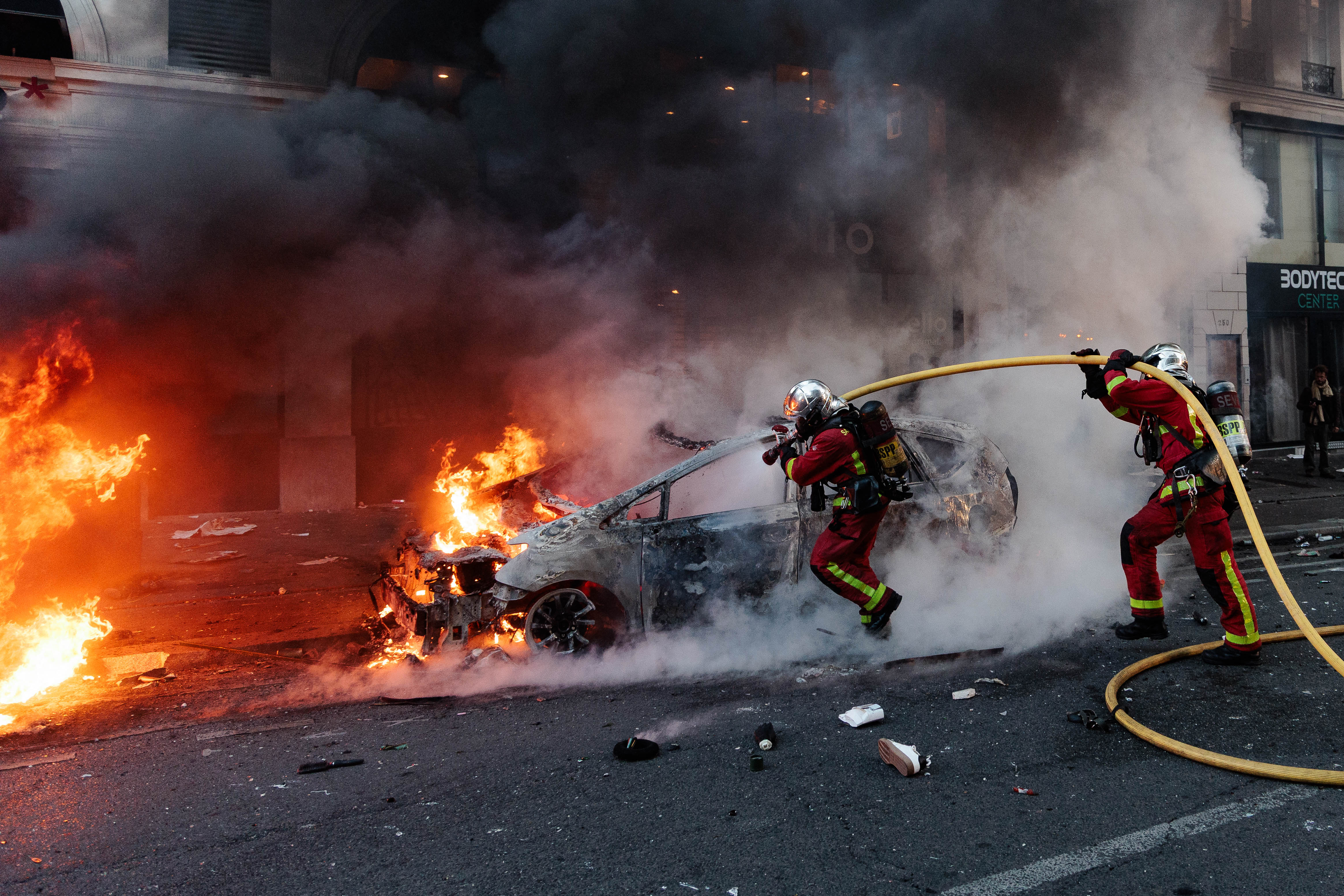 Firefighters respond to extinguish a car fire during violent clashes on the fringes of a protest in Paris