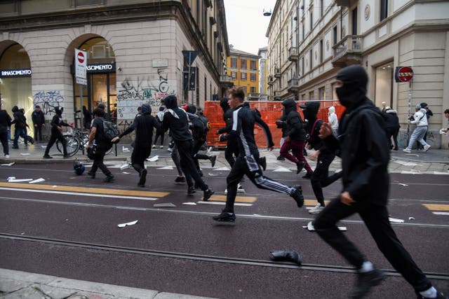 Protesters run along a street strewn with debris during a protest over the state of public services and the rising cost of living in Milan, on Sunday