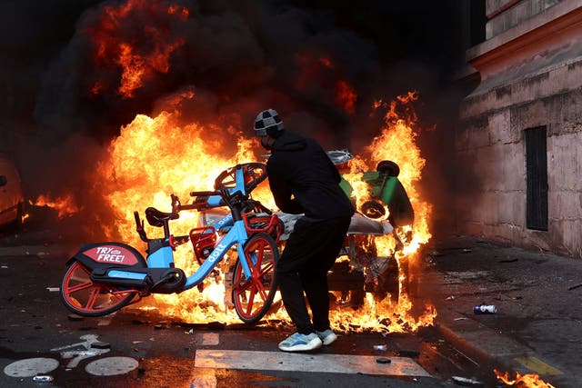 A protester throws a bicycle onto a burning car amid clashes during a day of demonstrations against the cost of living and rising fuel prices in Paris.