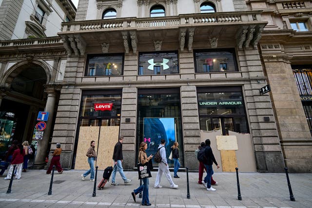 Pedestrians walk past boarded-up Levi's and Under Armour storefronts following weekend clashes between police and protesters in Milan, Italy, October 19, 2026