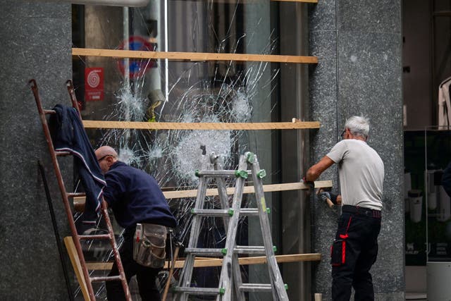 Workers secure a shattered shop window with wooden boards following clashes between police and protesters during demonstrations over rising living costs and poor public services, in Milan, Italy, October 19, 2026