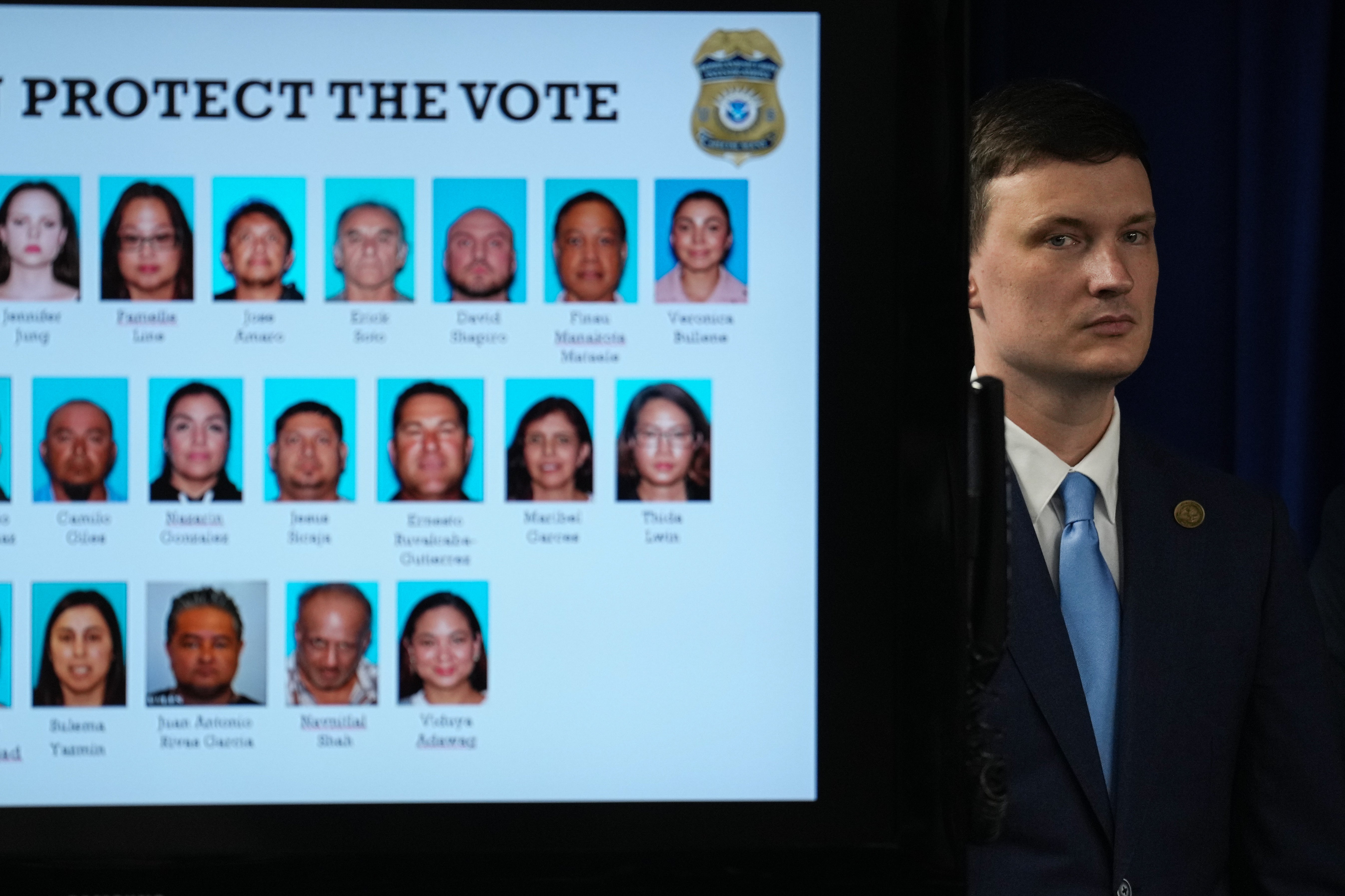 Acting U.S. Deputy Attorney General Trent McCotter stands next to a display showing photos of people charged with illegally registering to vote during a news conference in Los Angeles