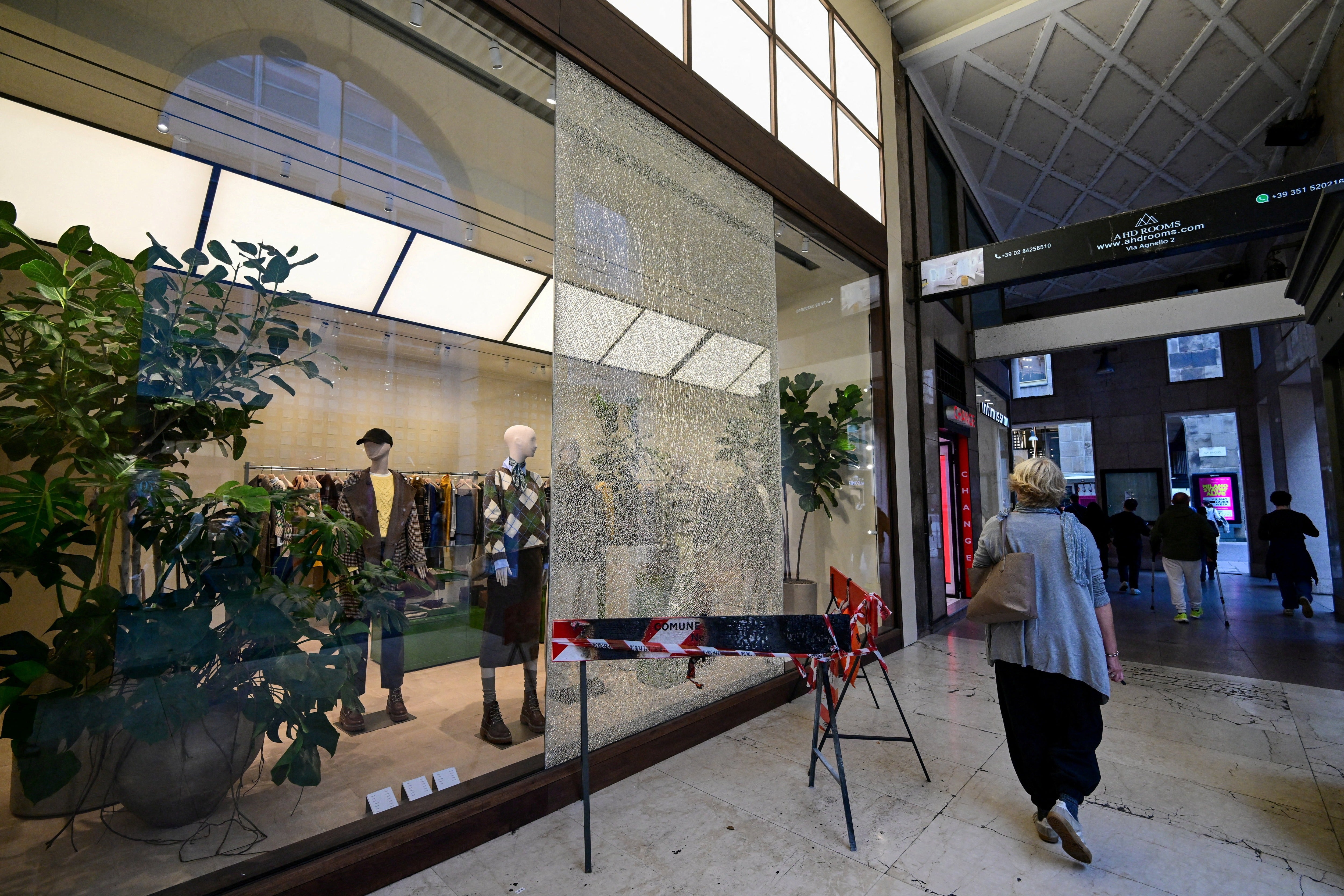 A woman walks past a shattered shop window cordoned off with safety barriers in a shopping passage following weekend clashes between police and protesters