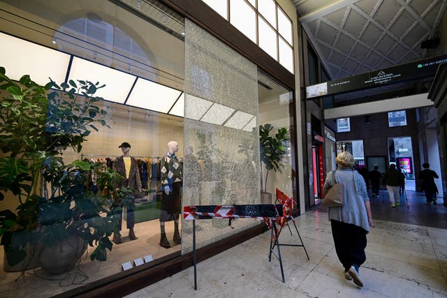 A woman walks past a shattered shop window cordoned off with safety barriers in a shopping passage following weekend clashes between police and protesters