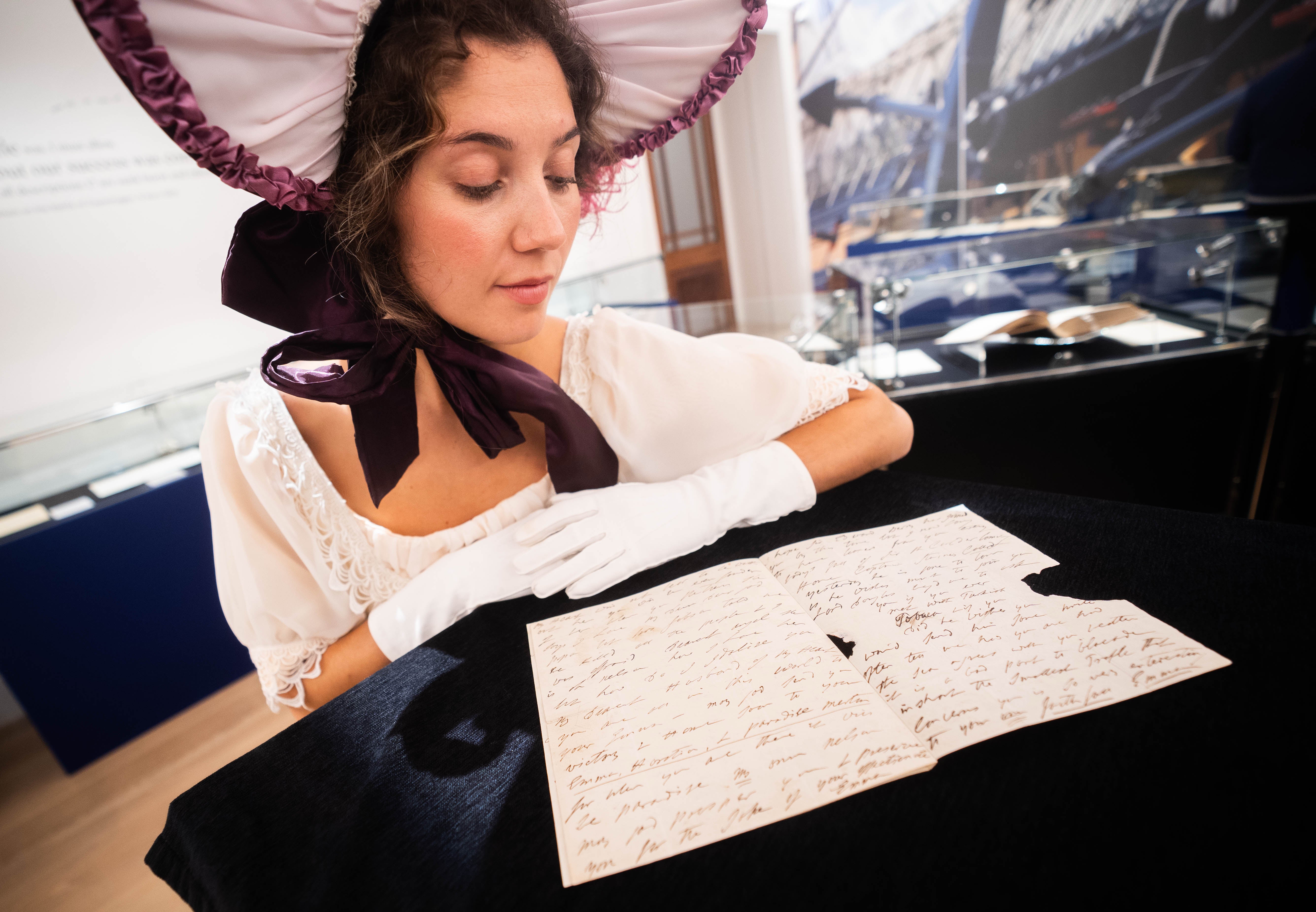 A lady in period costume looks at a letter written by Emma Hamilton sent to Lord Nelson which arrived after his death
