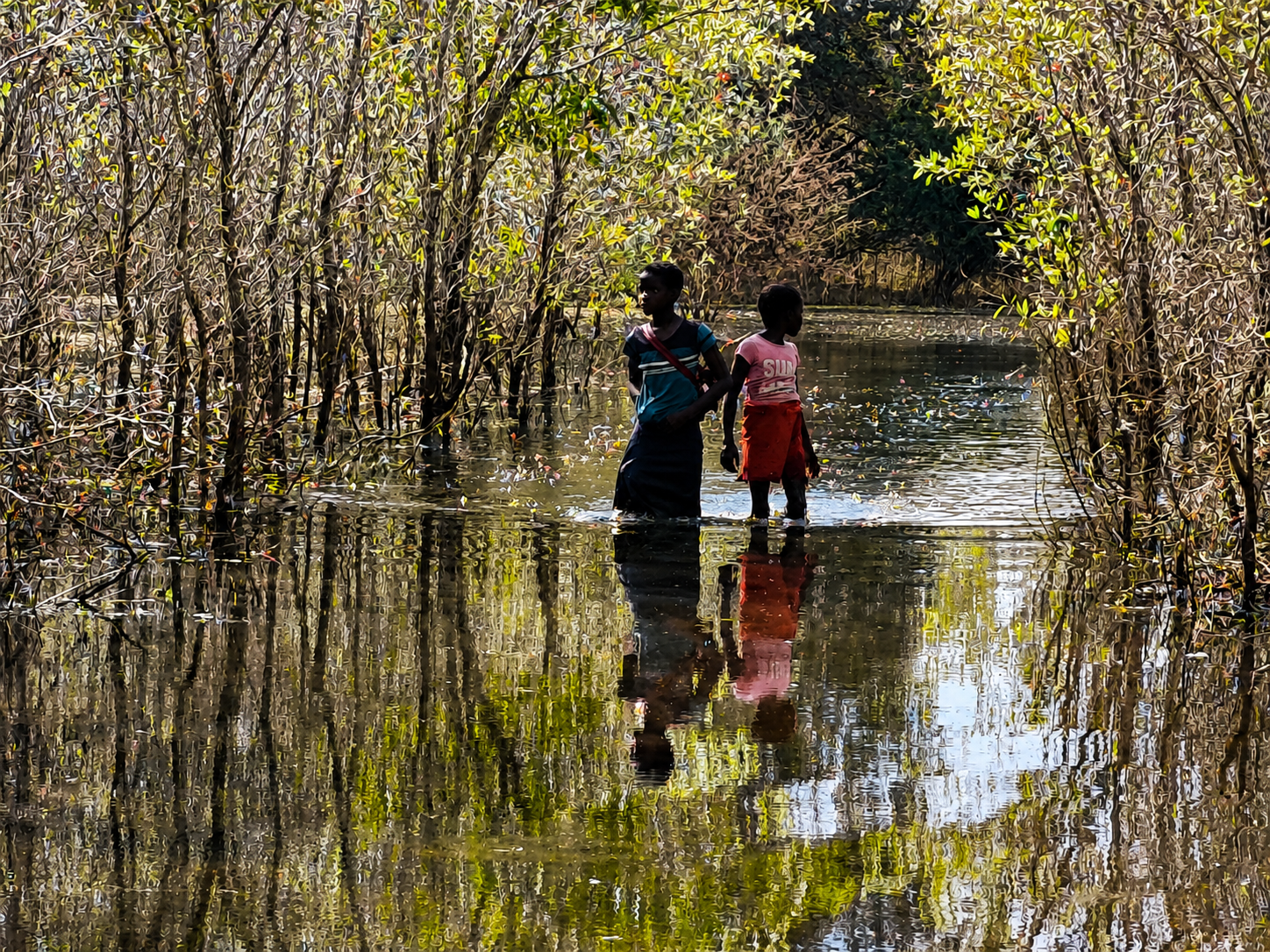 Two children walk through floodwaters to reach school in Nalaze, Mozambique, six months after severe flooding left children facing continued barriers to their education